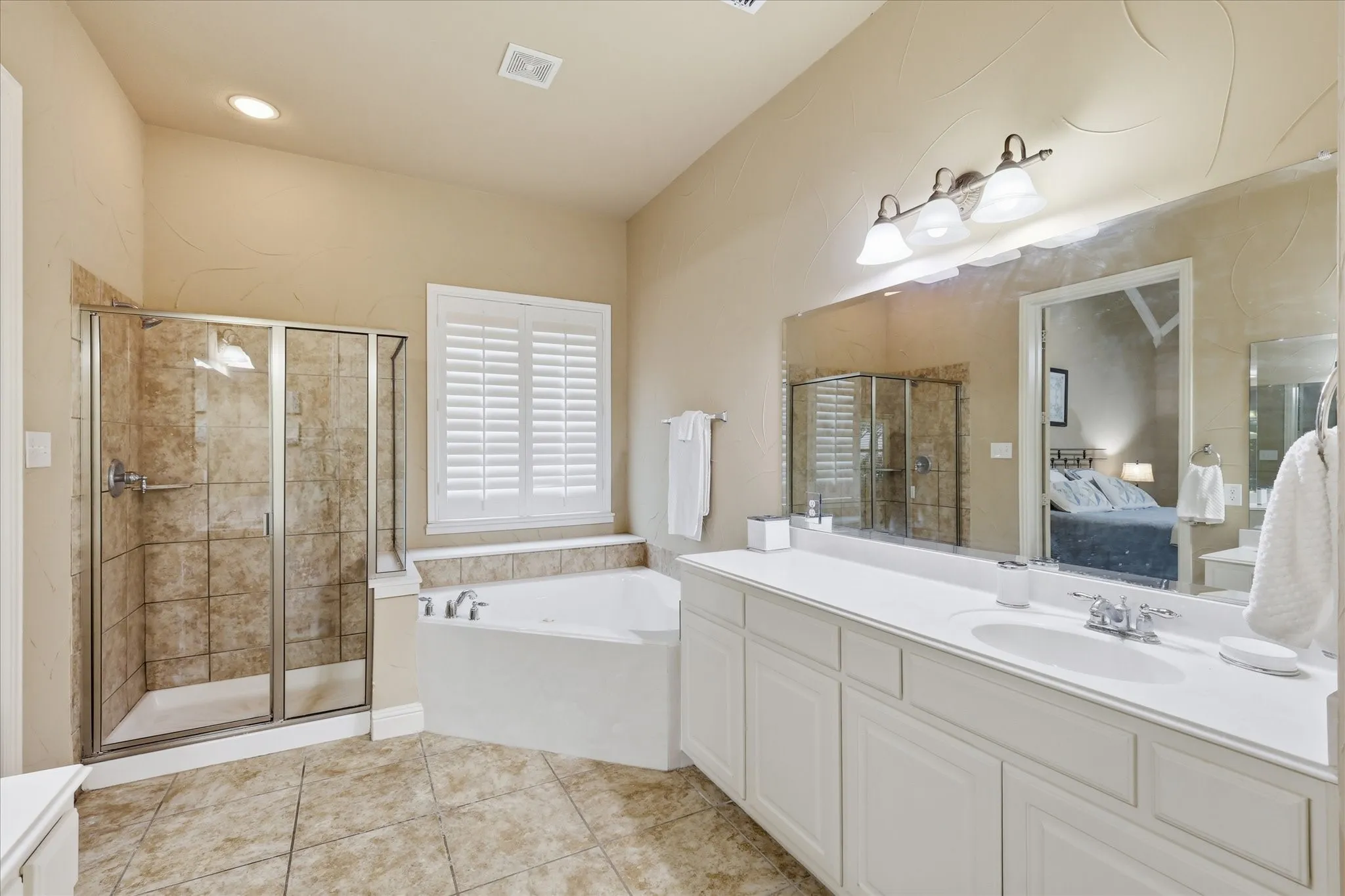Spacious bathroom featuring a dual-sink vanity with white cabinetry, a separate walk-in shower with glass enclosure, a built-in soaking tub, and ceramic tile flooring