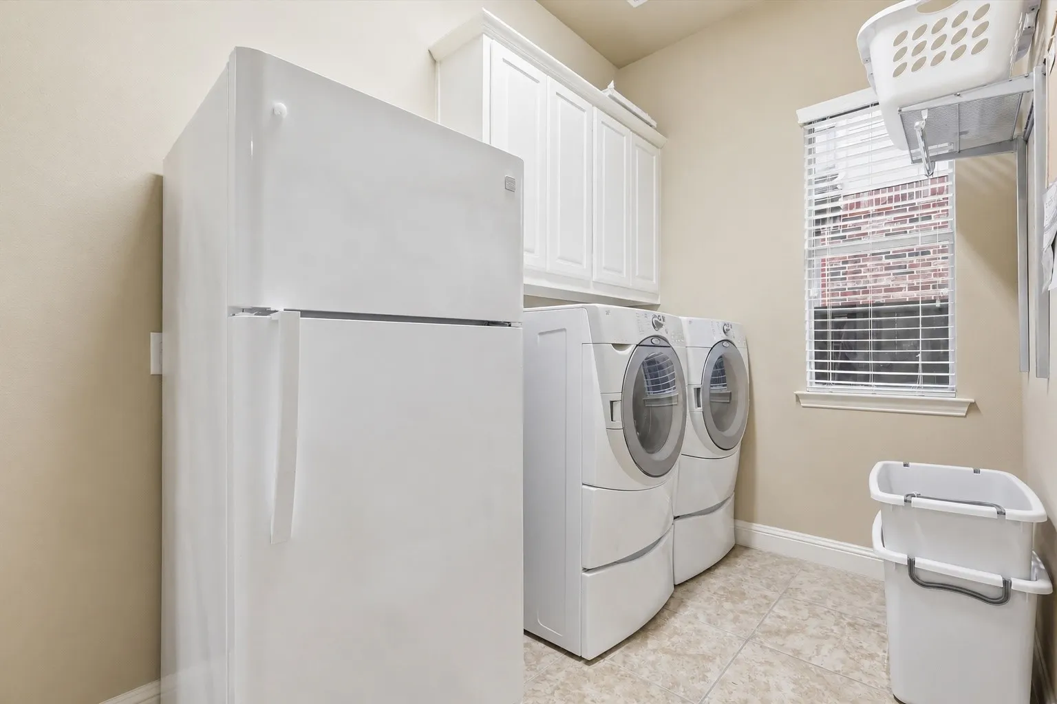 Dedicated utility room featuring a large refrigerator, front-loading washer and dryer, upper cabinetry, and tiled flooring