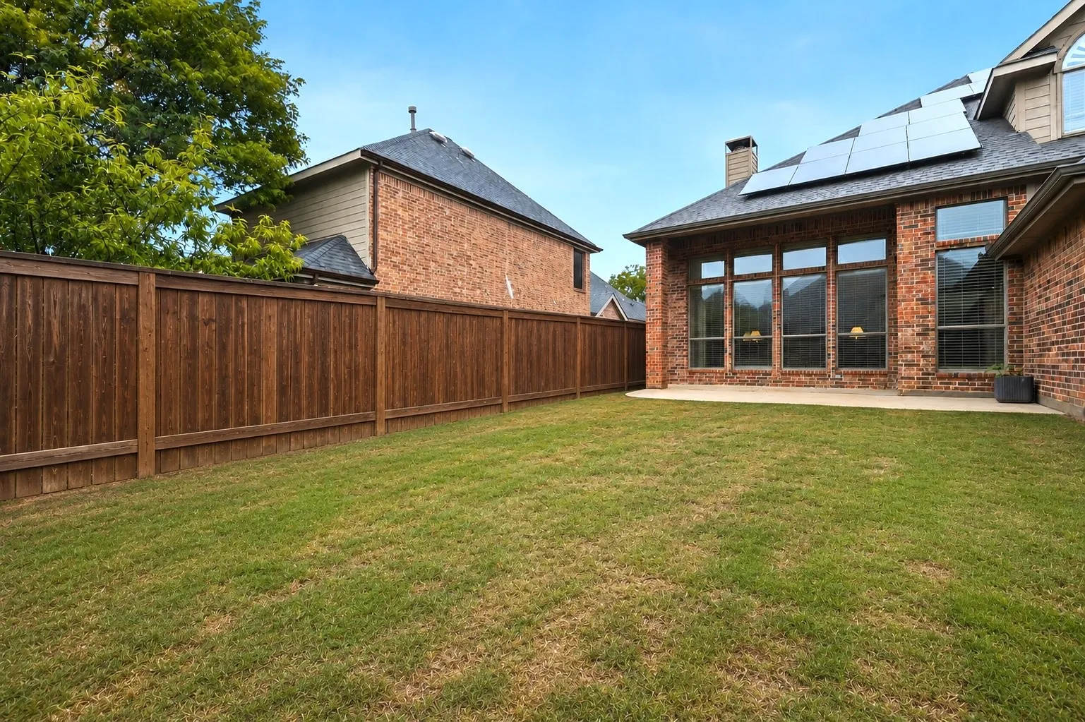 Expansive backyard featuring a lush lawn, solid wood privacy fencing, and a brick exterior with a rear patio