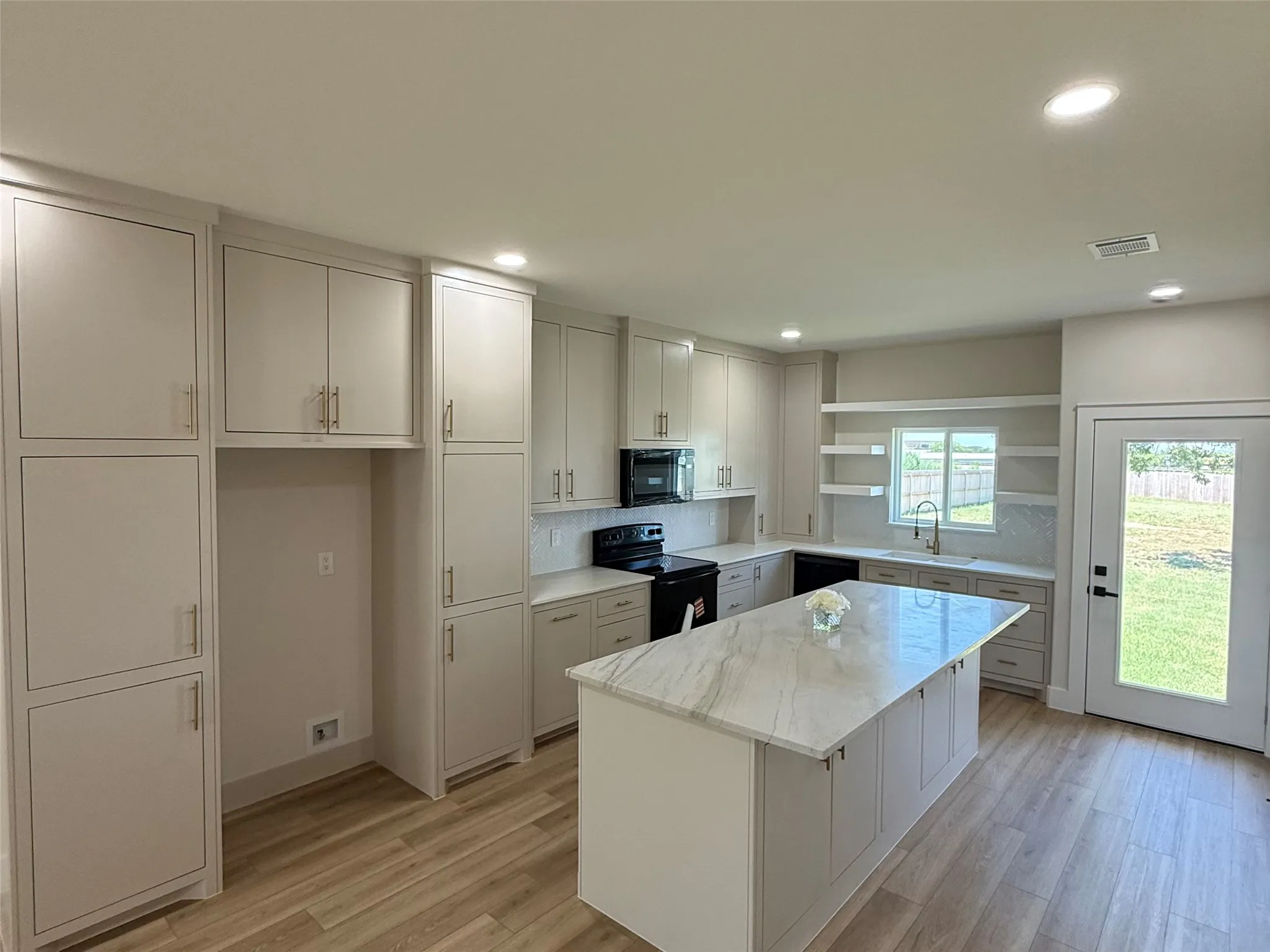 Bright kitchen featuring a large center island with a stone countertop, extensive cabinetry, wood-finish flooring, recessed lighting, and a glass-paneled exterior door