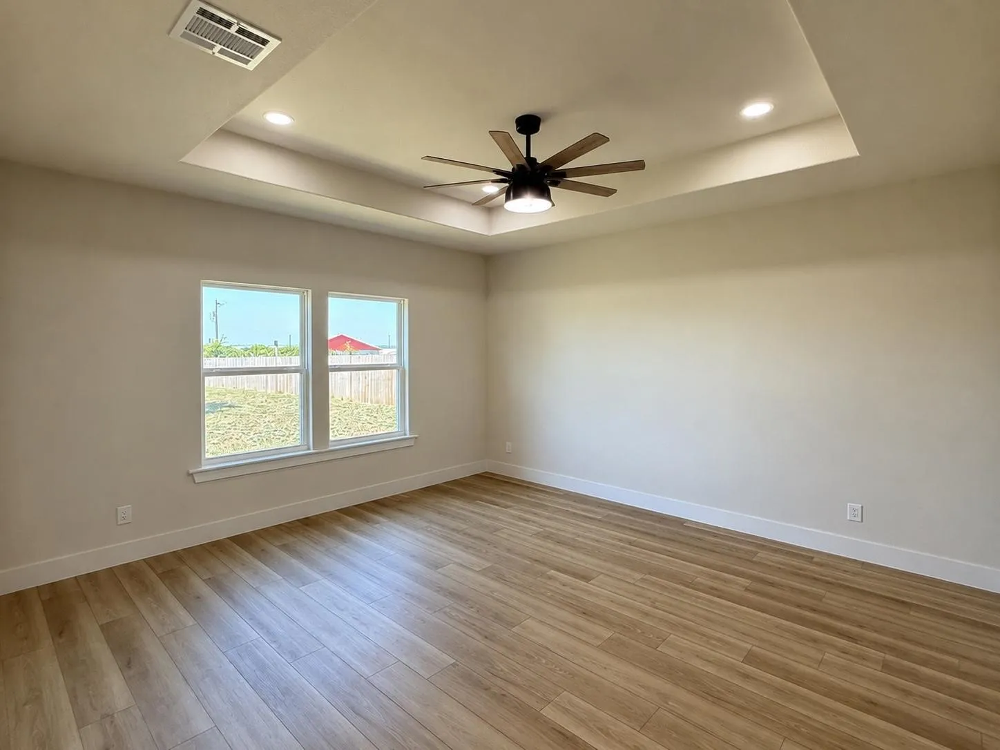 Spacious primary suite with an elegant tray ceiling with recessed lighting, a modern ceiling fan with integrated lighting, and two large windows