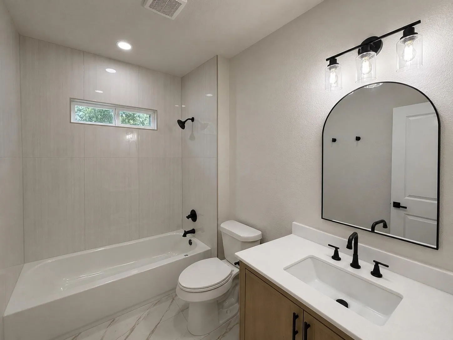 Full bathroom featuring a single vanity with a white countertop and undermount sink, a sleek black faucet, and an arched mirror