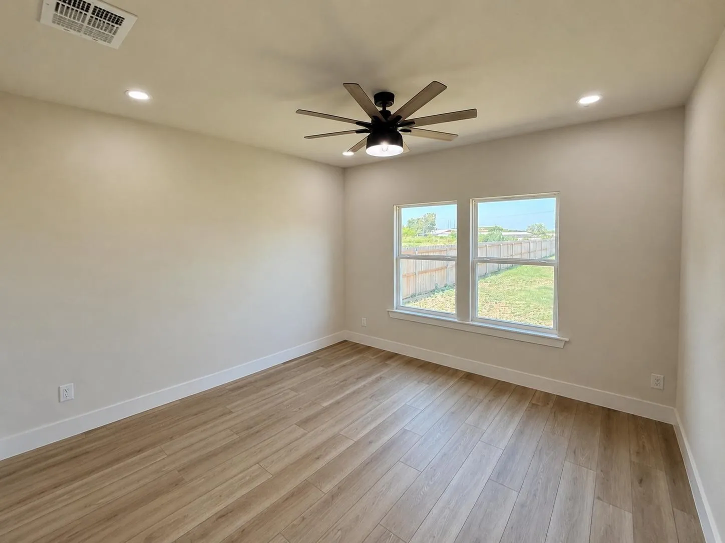 Room featuring wood-finish flooring, two large windows, a ceiling fan with integrated lighting, recessed lighting, and crisp white baseboards