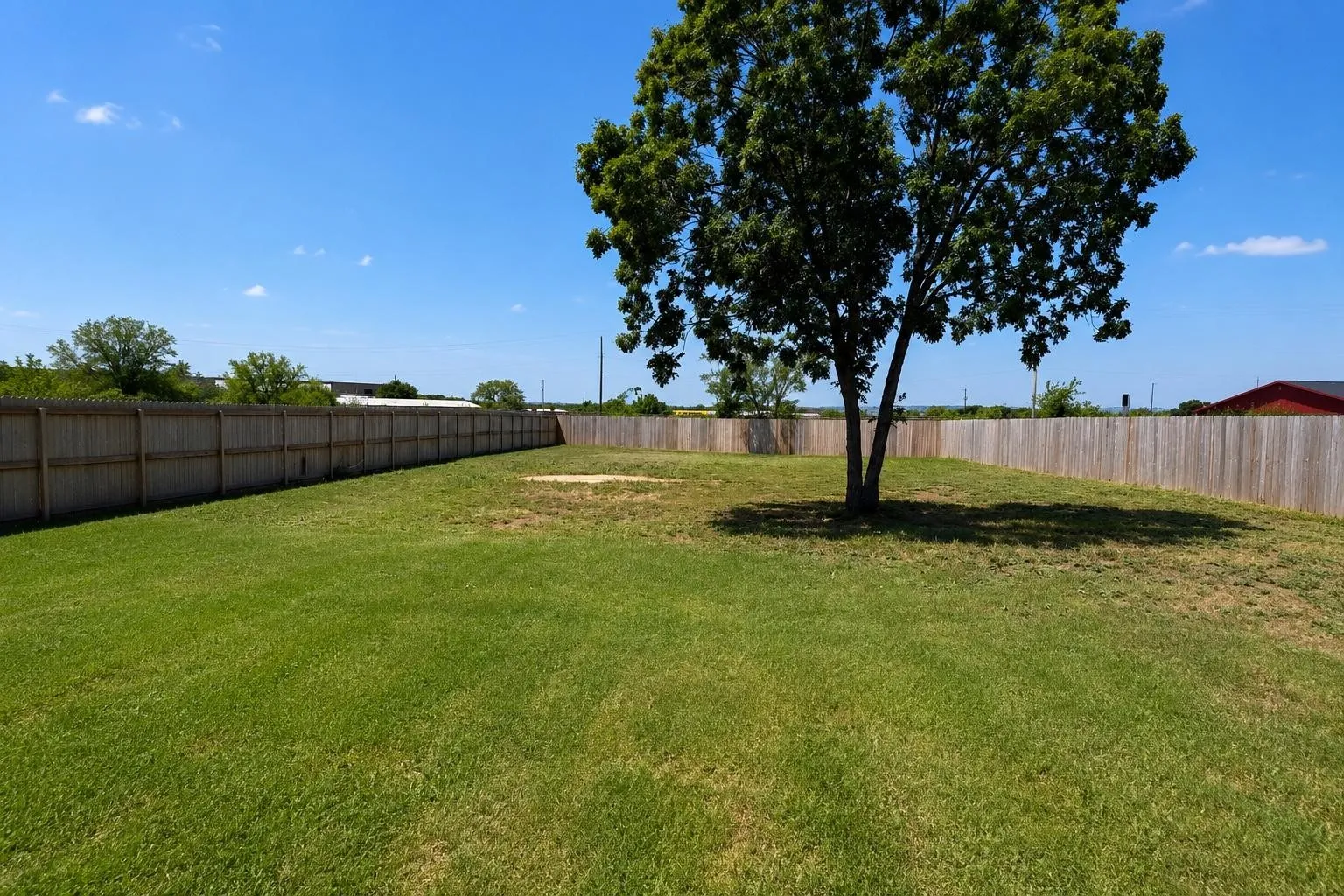 Expansive rear yard featuring a privacy fence, mature shade tree, and a large grassy area