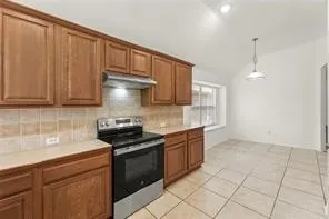Kitchen featuring wood-finish cabinetry, light-toned countertops, a tile backsplash, and a stainless steel and black range with an overhead vent hood