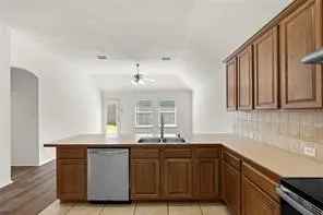 Kitchen featuring wood cabinetry, a stainless steel dishwasher, double basin sink, and tile flooring