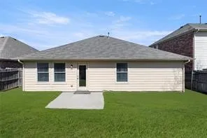 Spacious backyard featuring a manicured lawn, concrete patio, tan horizontal siding, and a gabled roofline