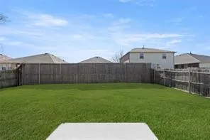 Expansive backyard featuring a lush green lawn, full perimeter wood fencing, and a concrete patio pad