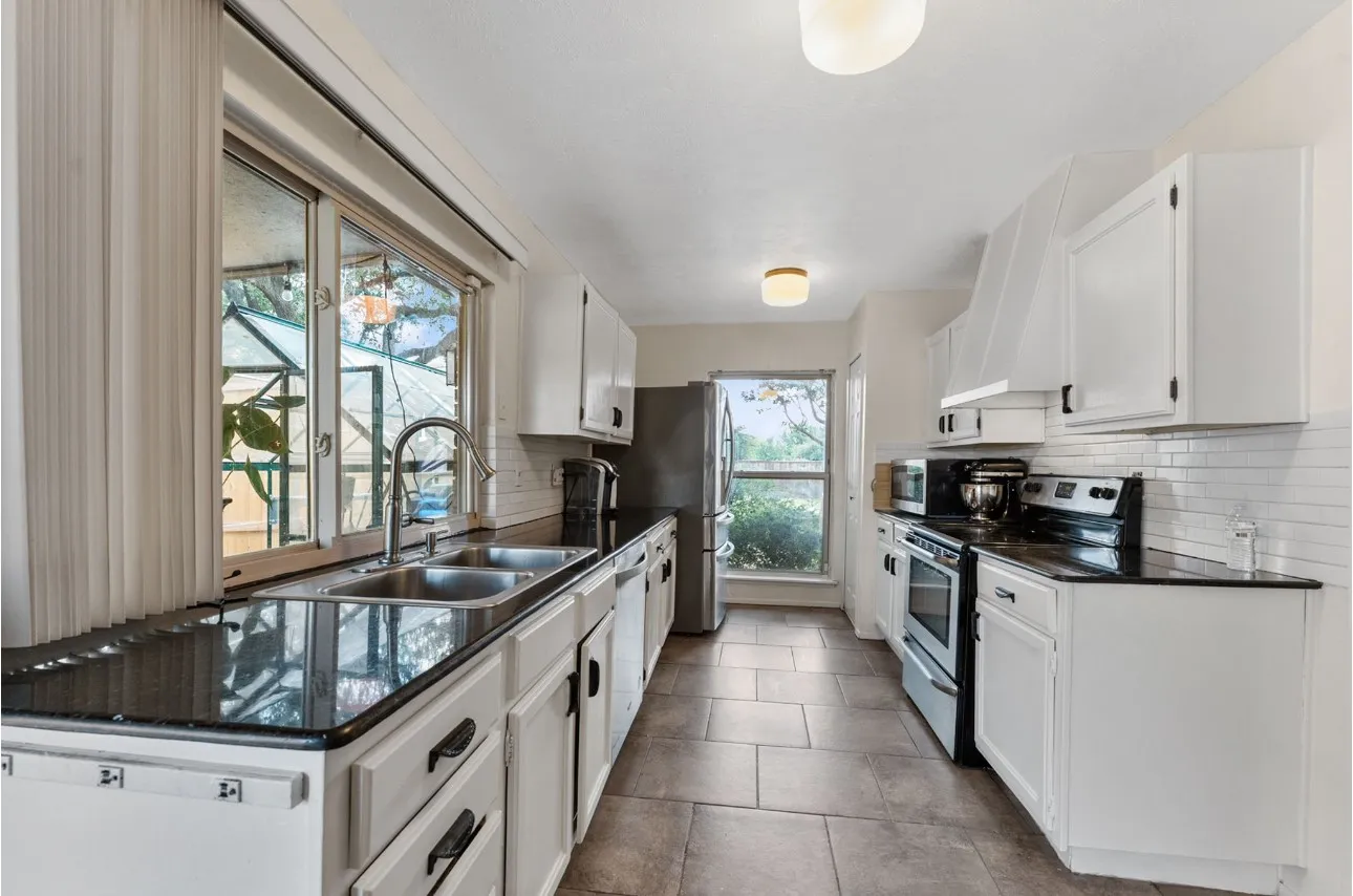 Kitchen featuring white cabinetry, black countertops, tile flooring, and a stainless steel double basin sink