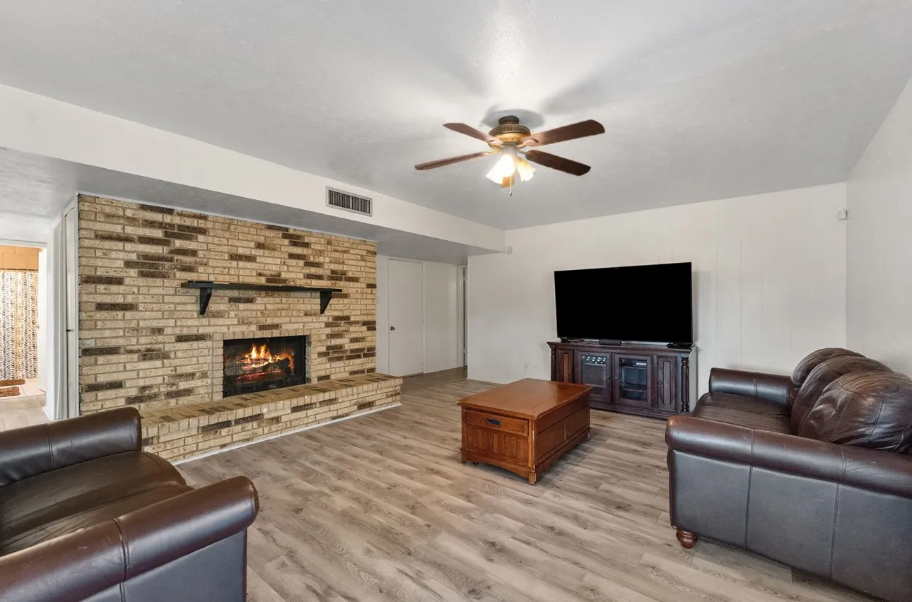 Brick-faced fireplace with a hearth, wood-finish flooring, and a ceiling fan with integrated lighting