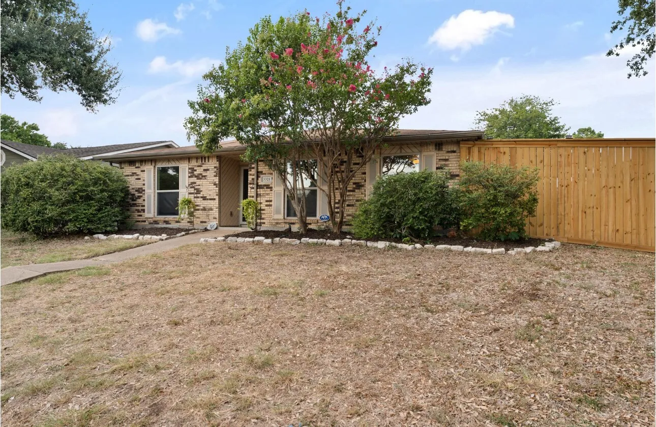 Brick exterior with contrasting trim, established landscaping, and a privacy fence