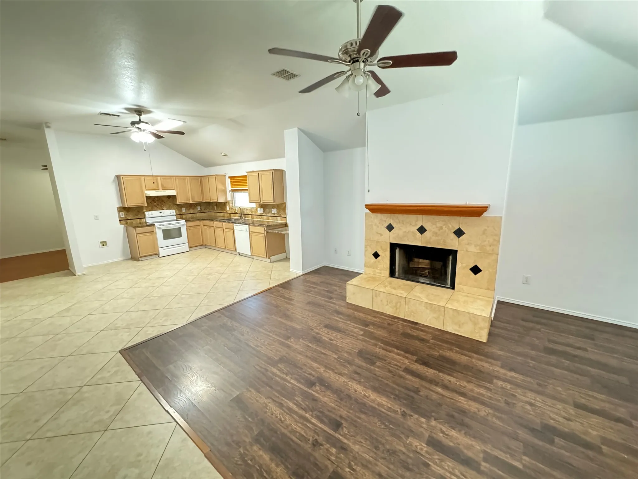 Unfurnished living room featuring a fireplace, light wood-type flooring, vaulted ceiling, and ceiling fan