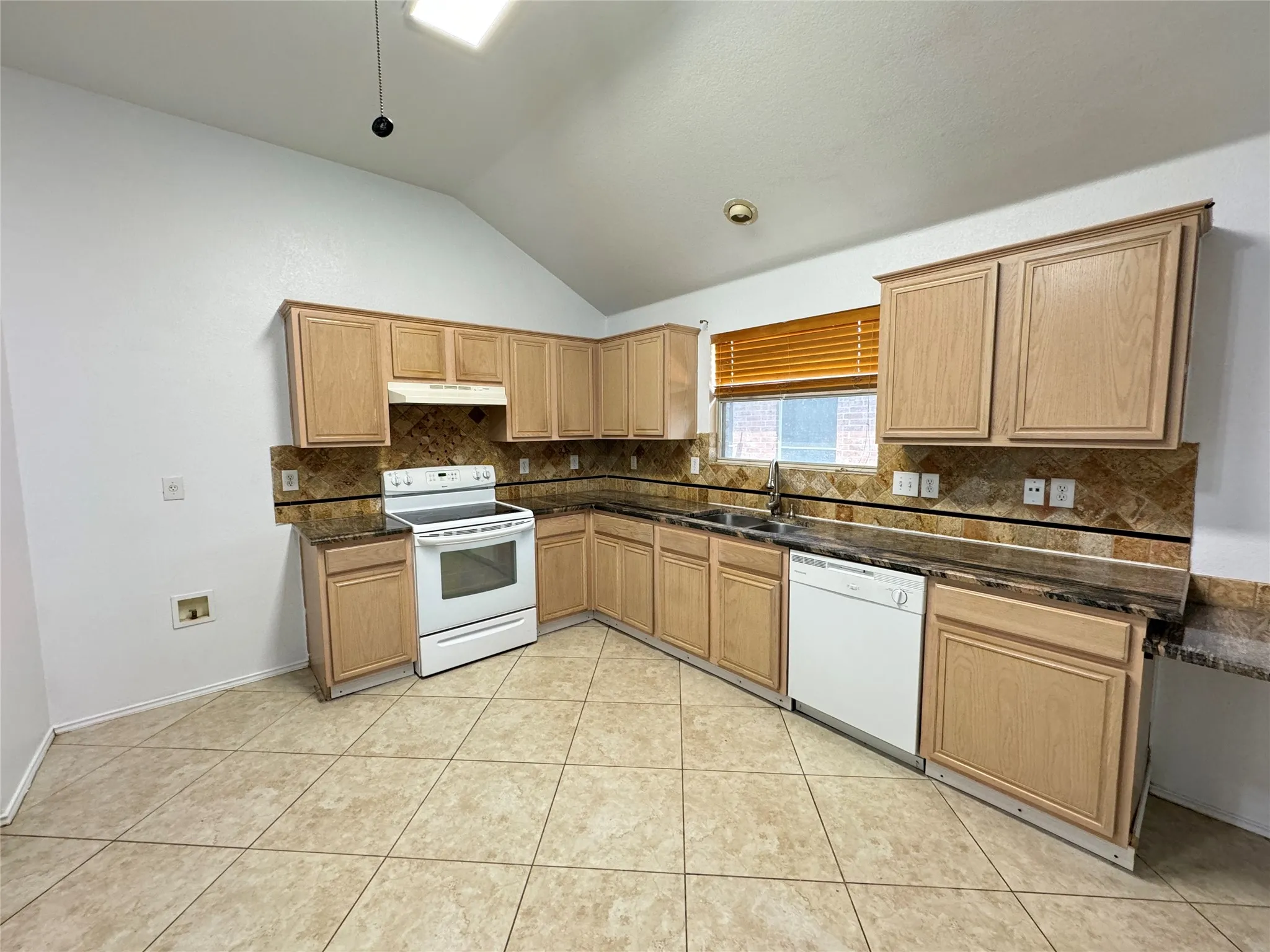 Kitchen with white appliances, sink, tasteful backsplash, light tile flooring, and vaulted ceiling