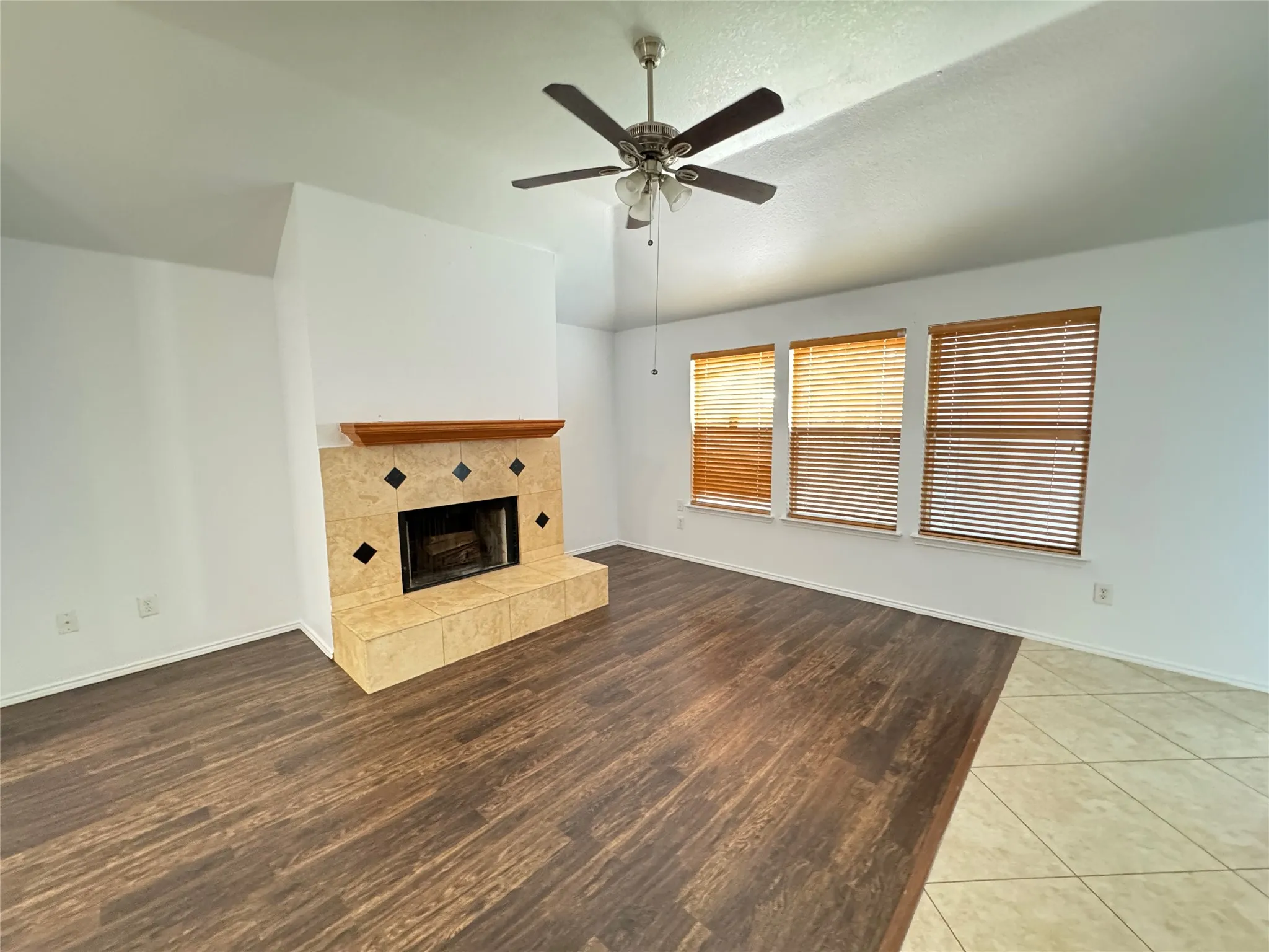 Unfurnished living room with ceiling fan, a tiled fireplace, and wood-type flooring