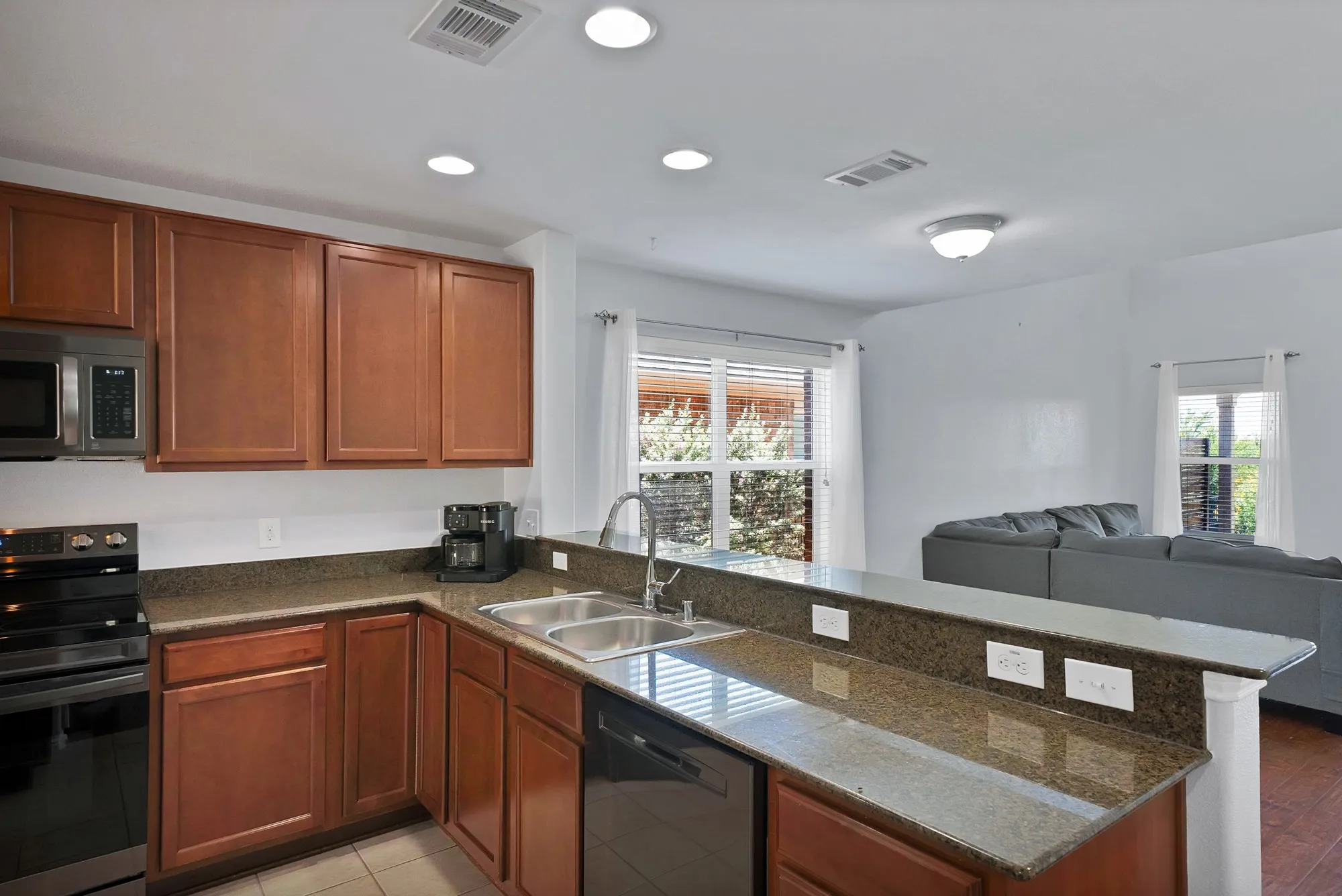 Kitchen featuring wood-finish cabinetry, granite countertops, double basin stainless steel sink, and stainless steel microwave