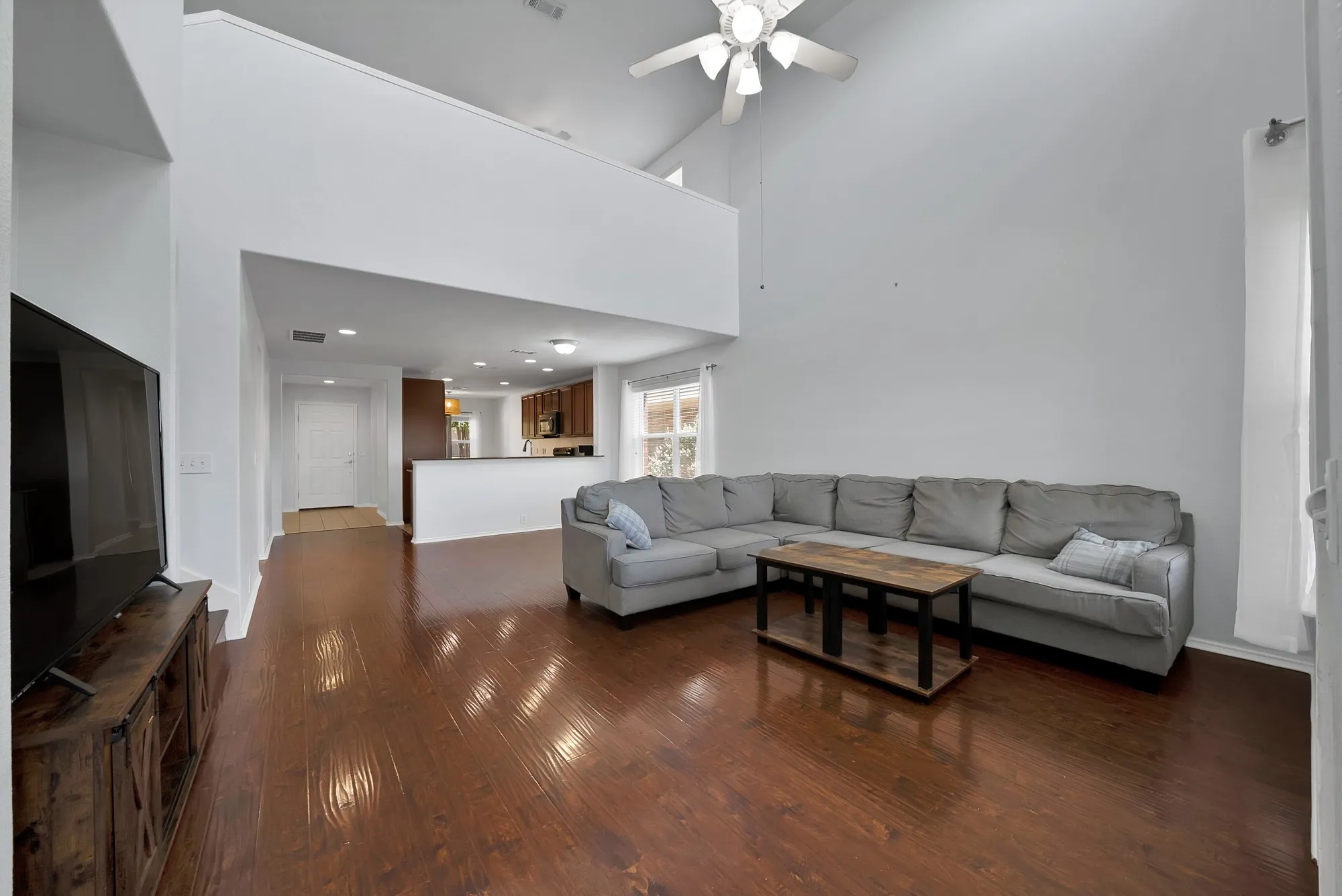 Open-concept living space featuring wood-finish flooring, vaulted ceilings, a ceiling fan, and a kitchen pass-through