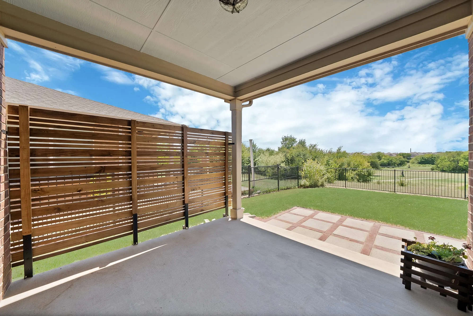 Covered patio featuring a concrete floor, slatted wood privacy fence, and brick detailing
