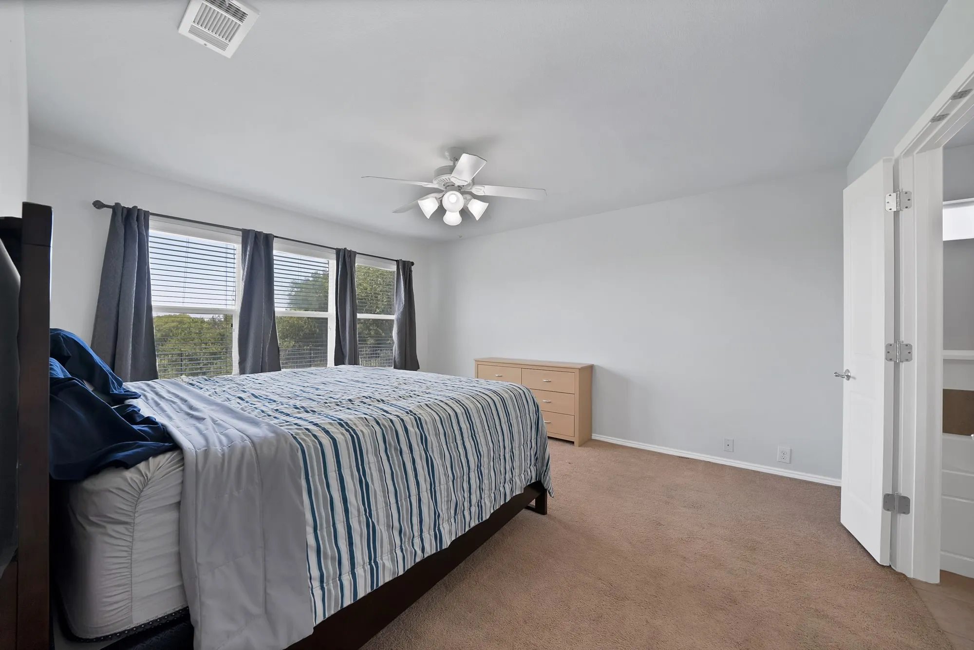 Carpeted room featuring multiple windows with blinds and draperies, a ceiling fan with integrated lighting, and a white interior door
