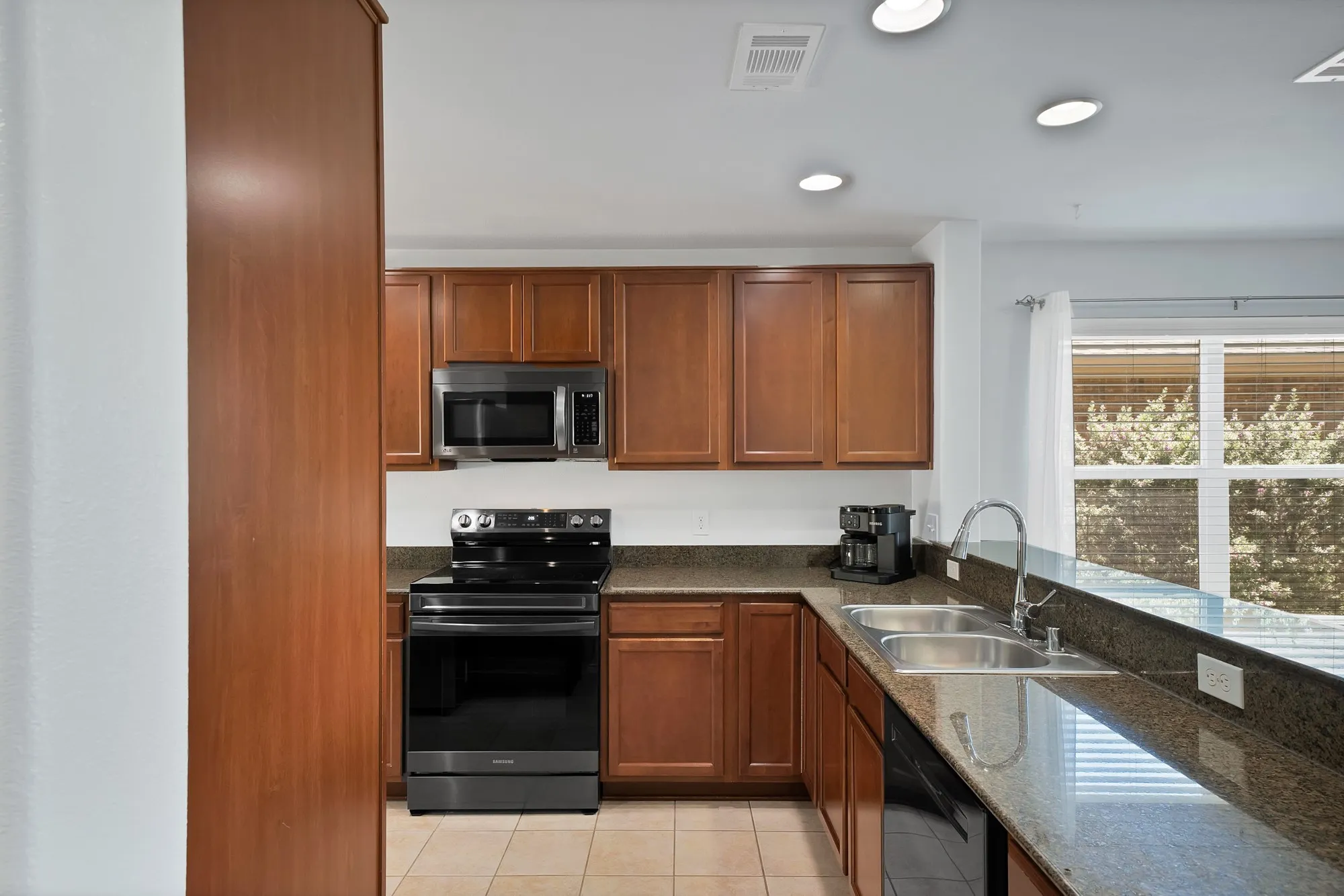 Kitchen featuring wood cabinetry, dark countertops, a stainless steel microwave, black electric range, and a double basin sink with a high-arch faucet