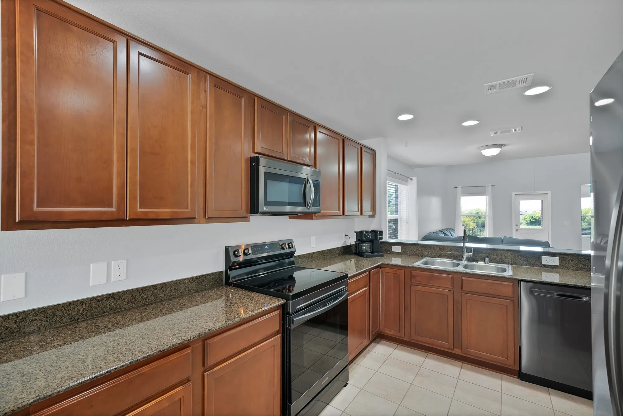 Kitchen featuring wood cabinetry, granite countertops, stainless steel appliances, and tile flooring