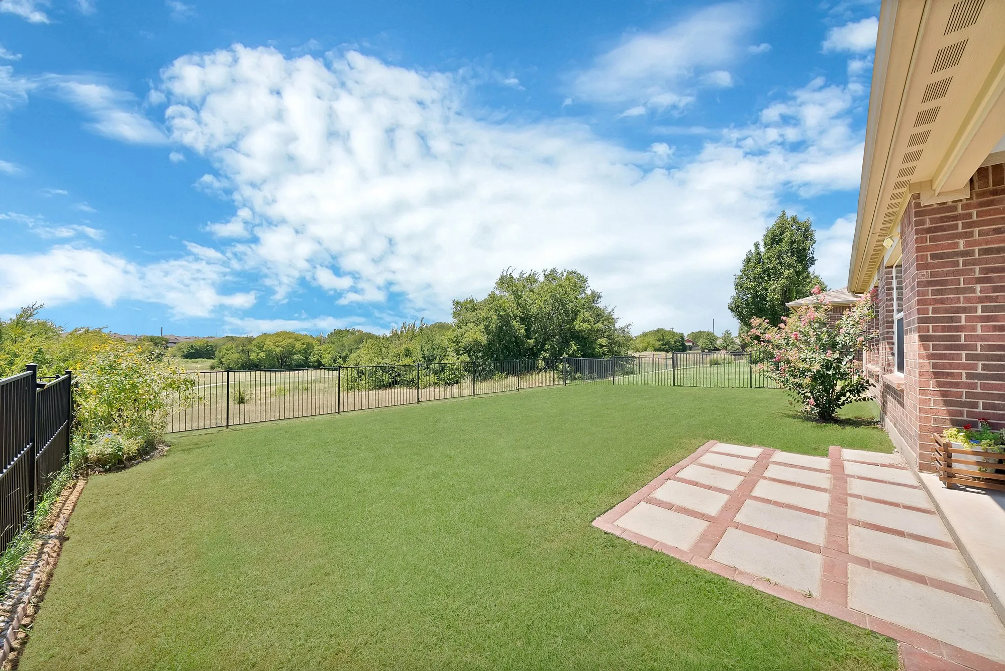Expansive backyard featuring a manicured lawn, full perimeter fencing, and a patterned paver patio