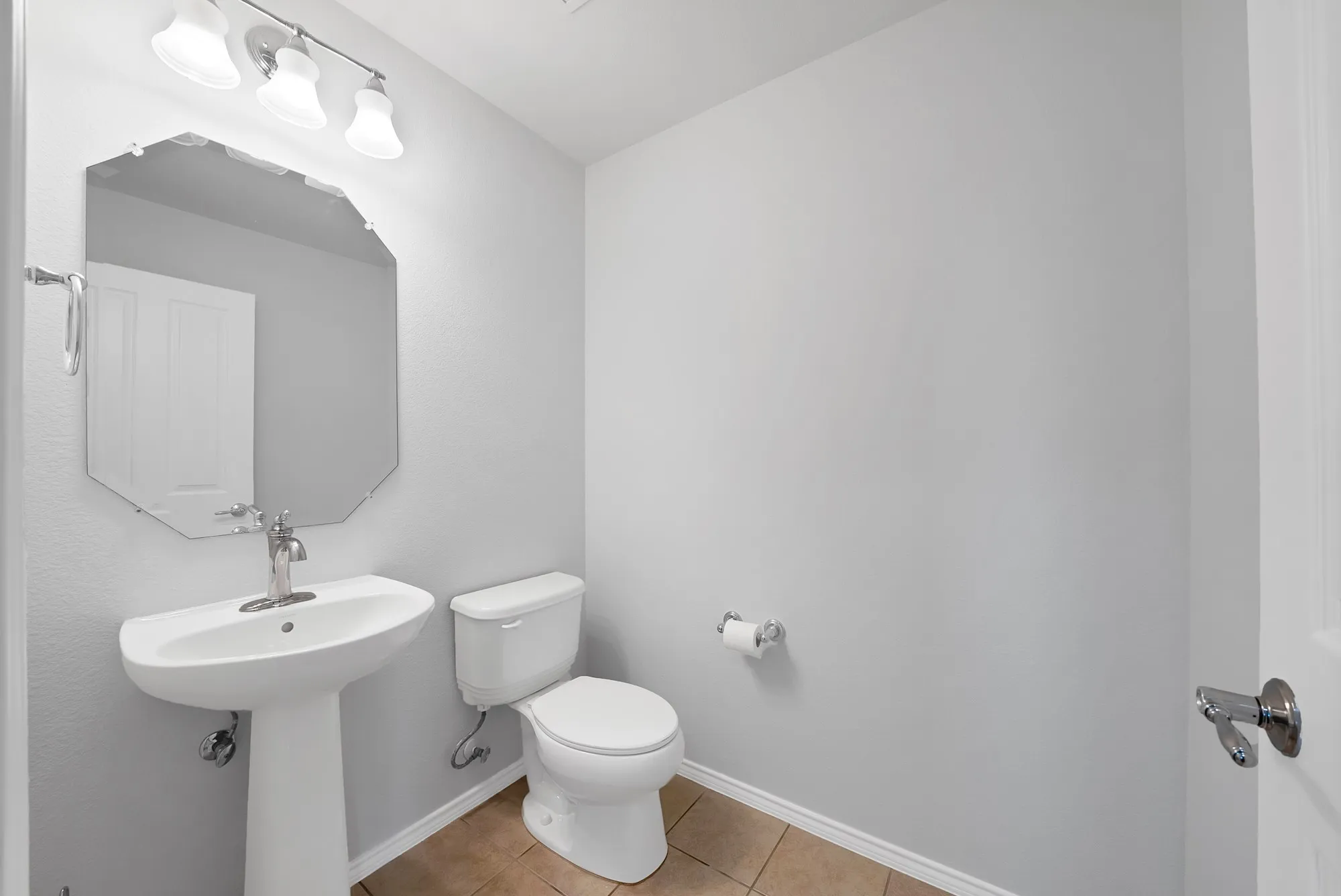 Powder room featuring a pedestal sink with a chrome faucet, an octagonal wall mirror, and a three-light vanity fixture