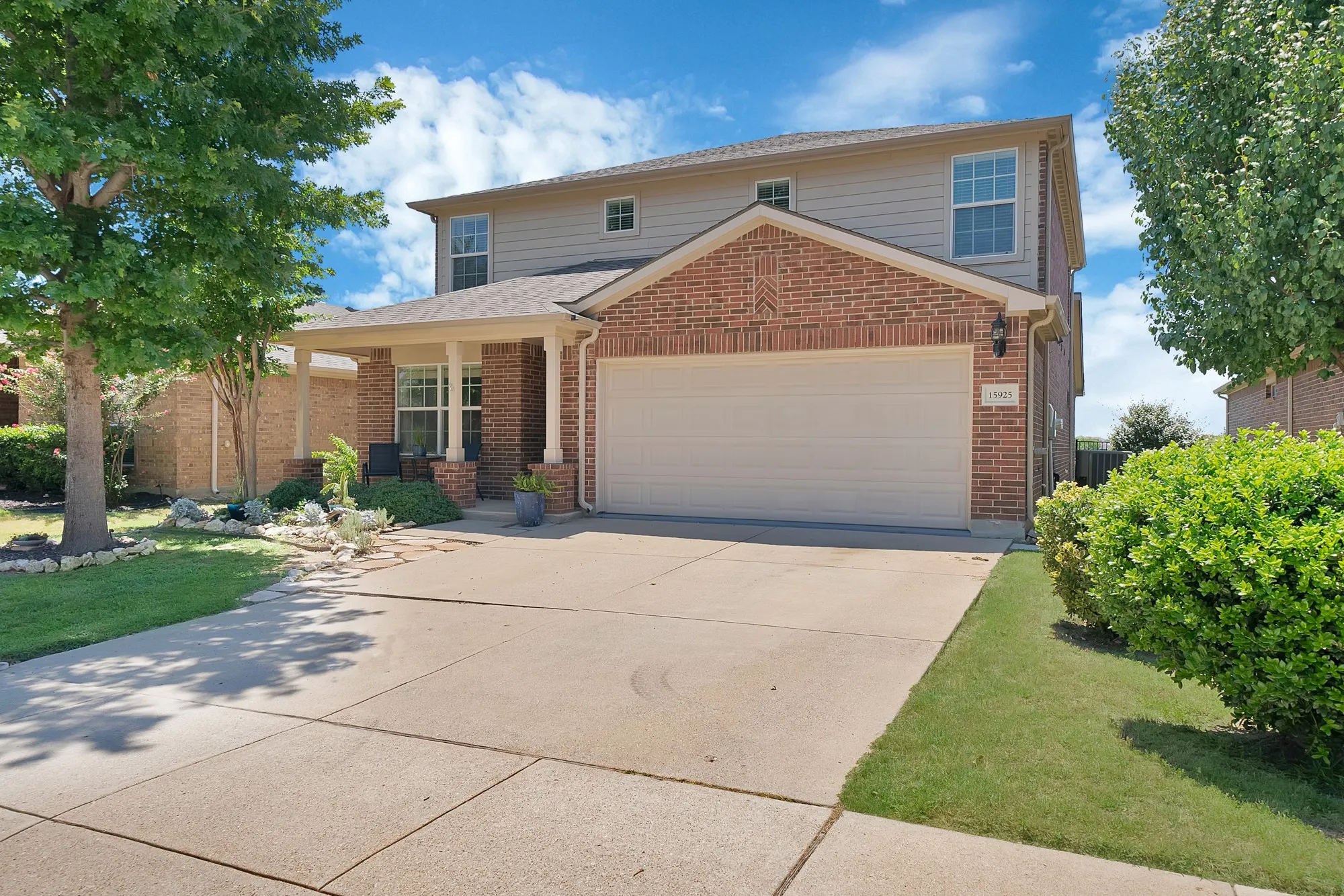 Brick and siding exterior featuring a covered front porch with columns, an attached garage, a concrete driveway, and established landscaping