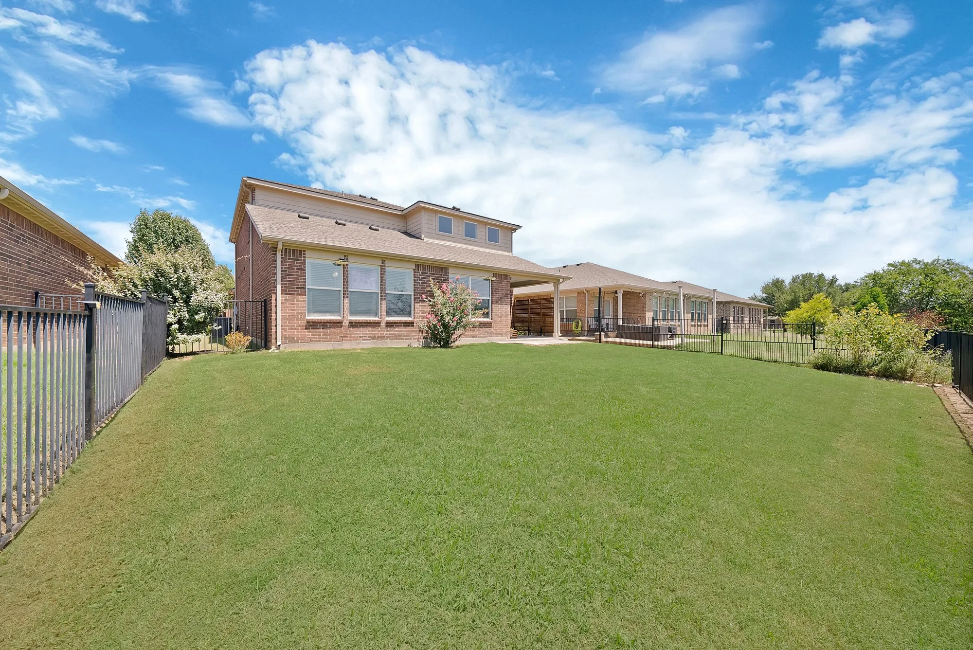 Expansive green lawn with a black metal fence enclosing the perimeter
