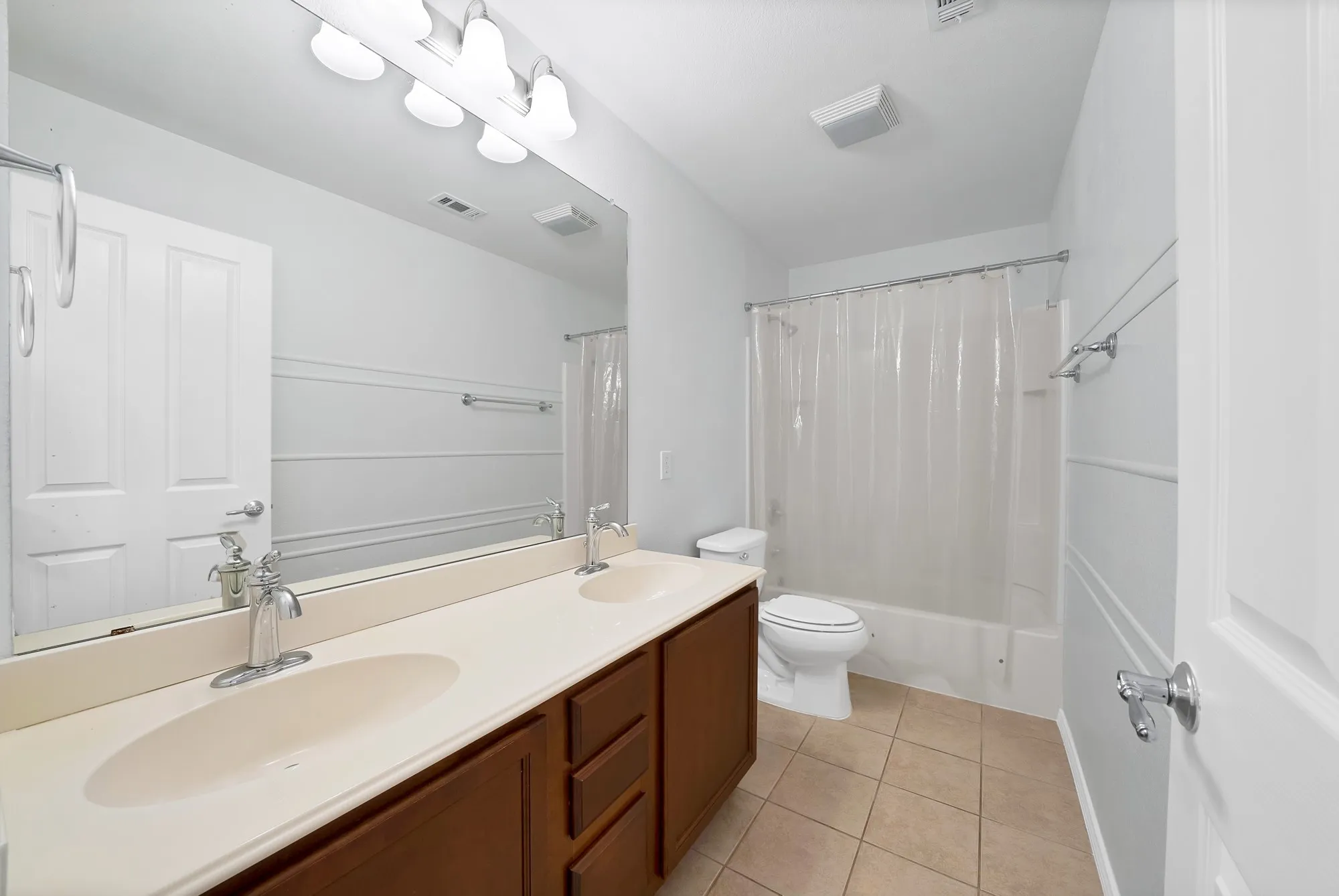 Bathroom featuring a dual vanity with a light-colored countertop and wood-finish cabinetry, a tub/shower combination, and ceramic tile flooring