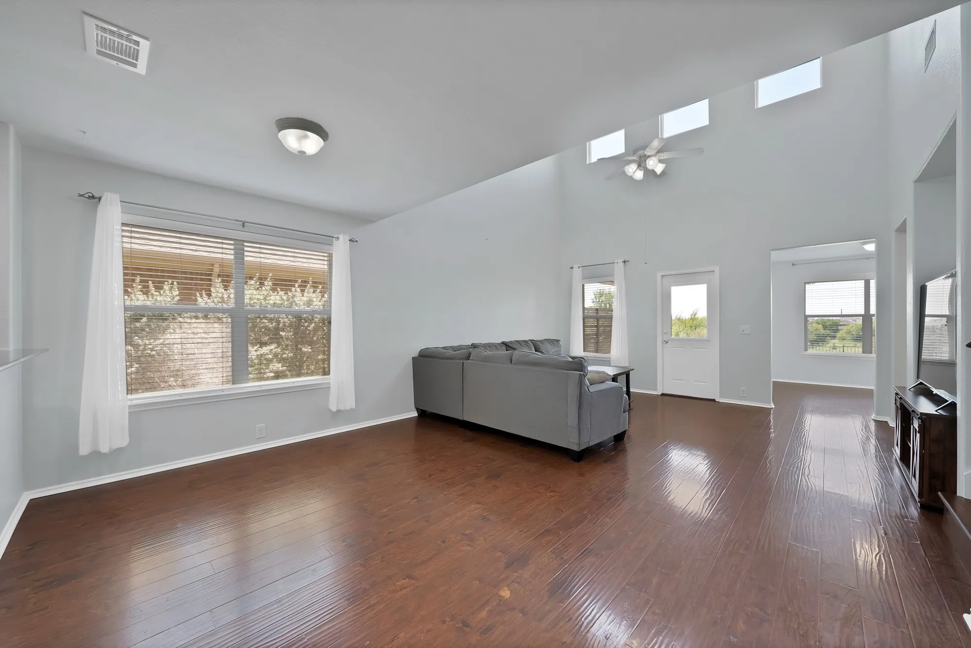 Living area featuring wood-finish flooring, high ceilings, multiple transom windows, ceiling fan, and direct exterior access