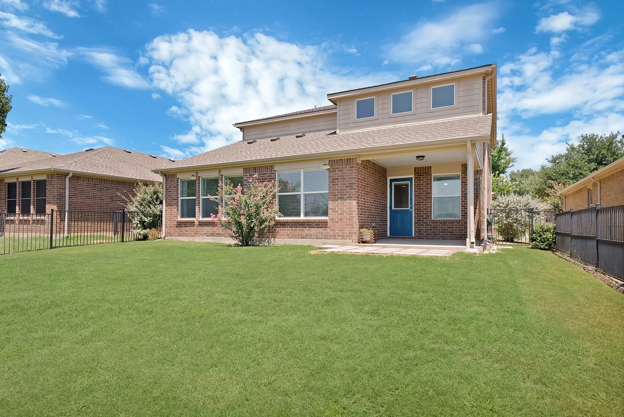 Expansive green lawn with a covered patio, brick exterior, and a blue rear entry door