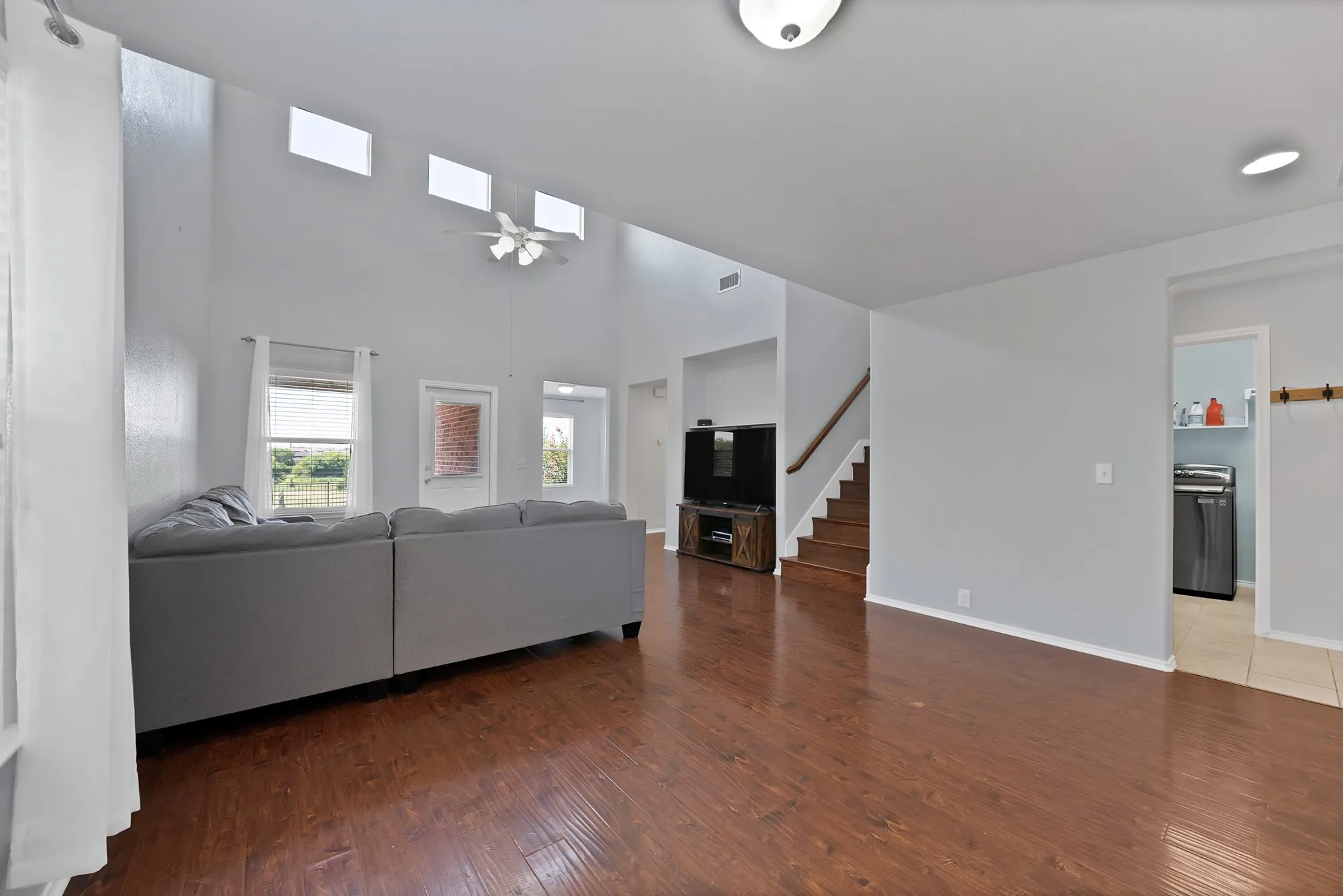 Open-concept living area featuring wood-finish flooring, a high vaulted ceiling, and multiple skylight windows