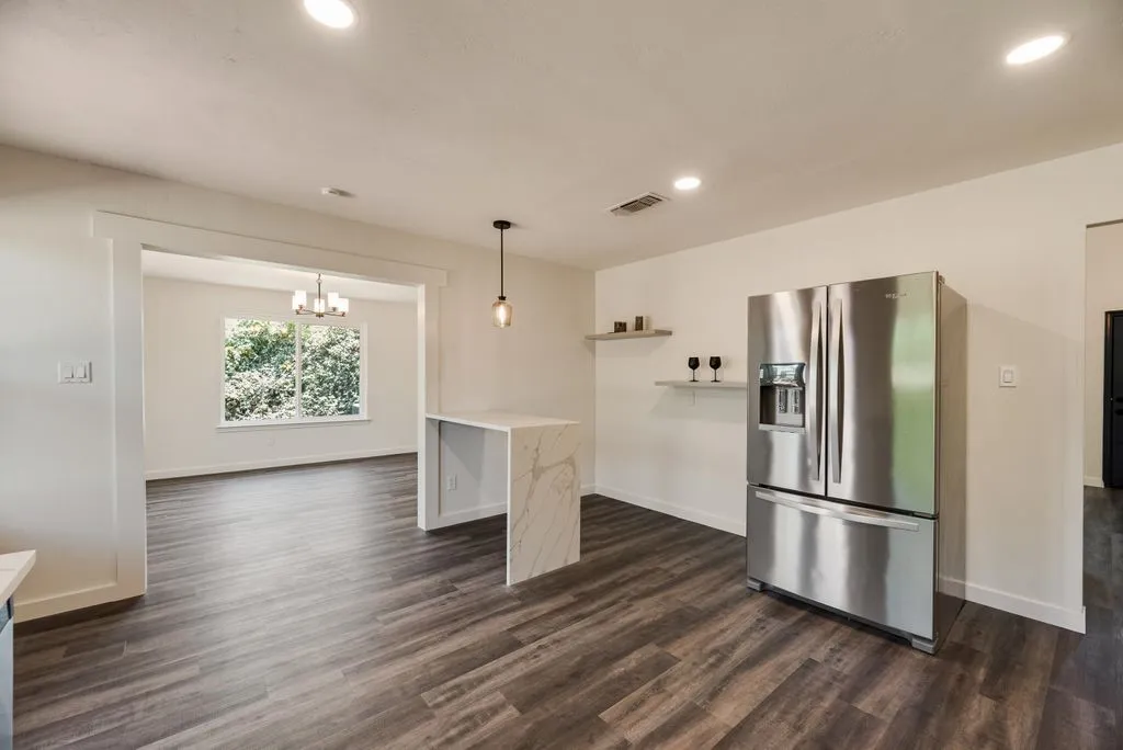 Open-concept living space featuring wood-finish flooring, recessed lighting, and a kitchen island with a waterfall countertop