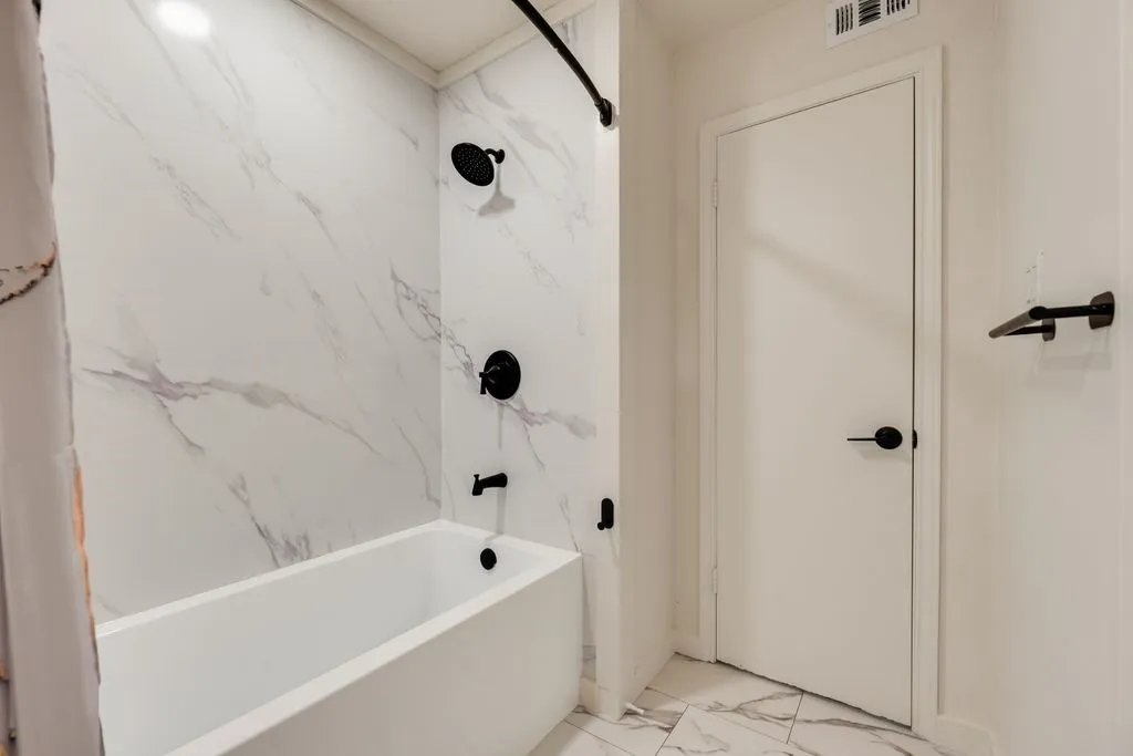 Bathtub with marble-patterned surround, matte black shower fixtures, and coordinating marble-patterned flooring