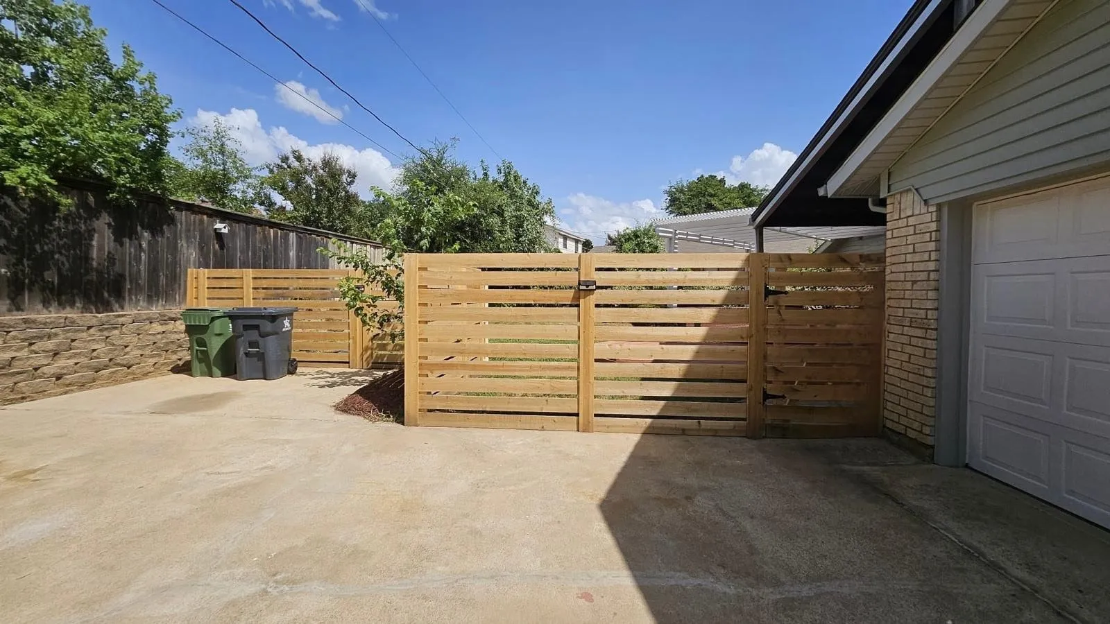 Private side yard area featuring horizontal slat fencing with a secure gate, a concrete pad, and a stone retaining wall