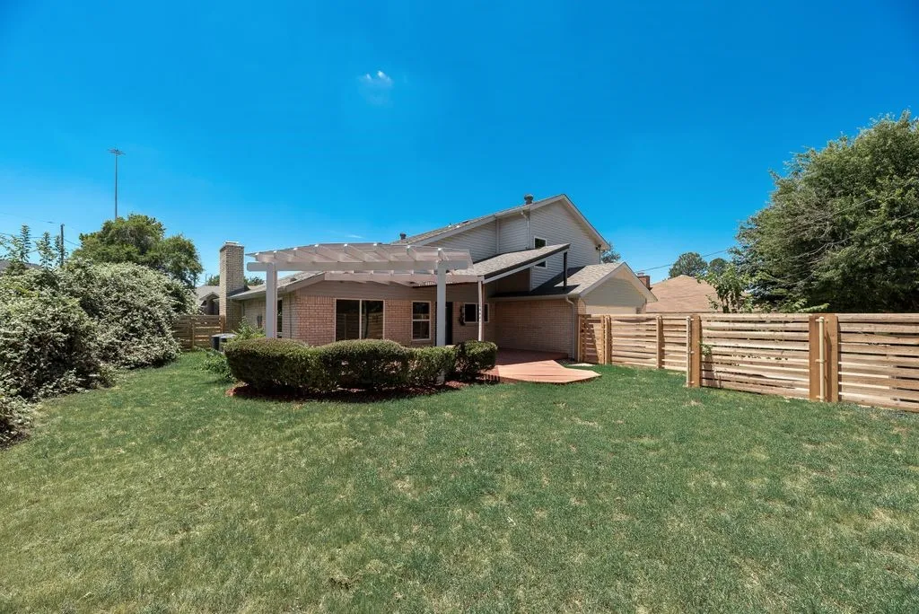 Expansive backyard featuring a manicured lawn, a detached pergola, and a brick patio