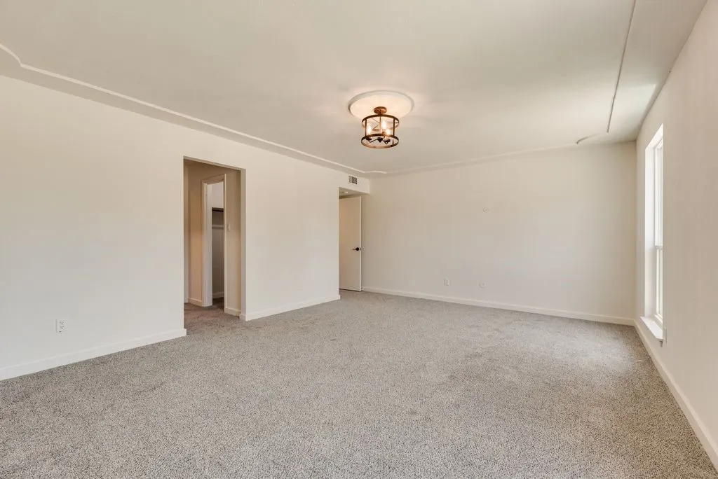 Spacious room featuring light gray carpeting, crown molding, a decorative ceiling light fixture, and white baseboards