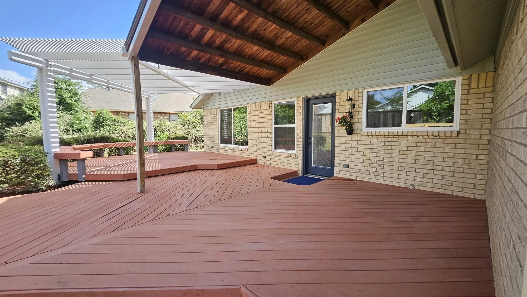 Multi-level wood-finish deck featuring integrated bench seating and a white slatted pergola