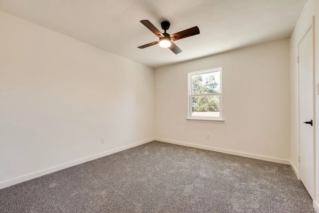 Bedroom featuring neutral wall paint, gray carpeting, a single window, white trim, and a ceiling fan with integrated lighting