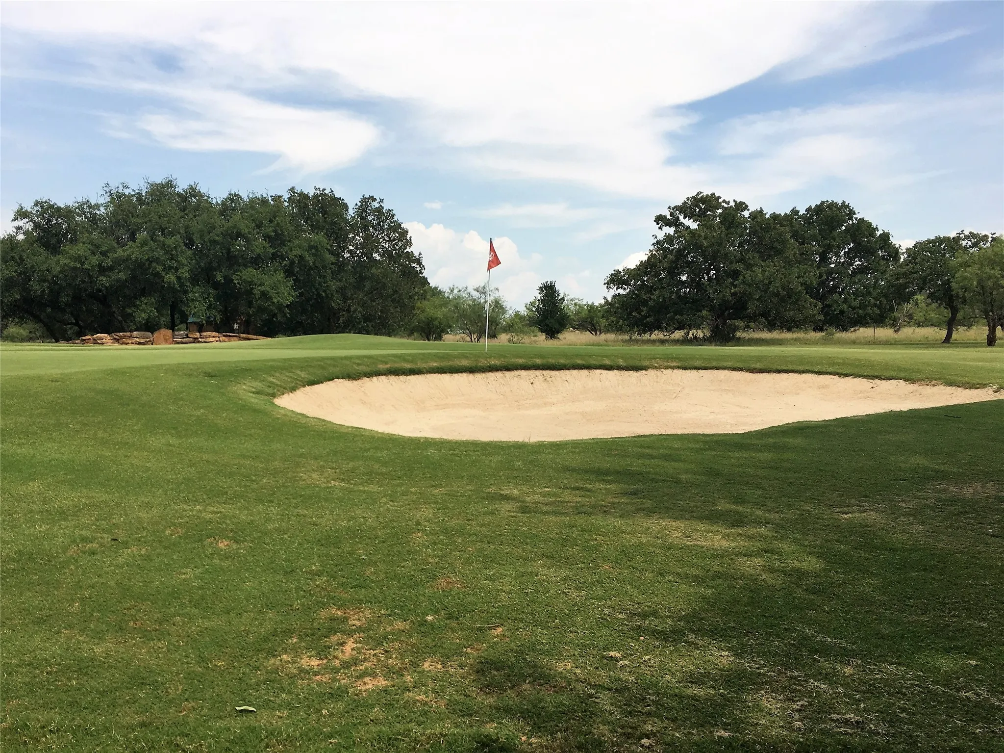 Golf course sand trap bordering a green with a red flag