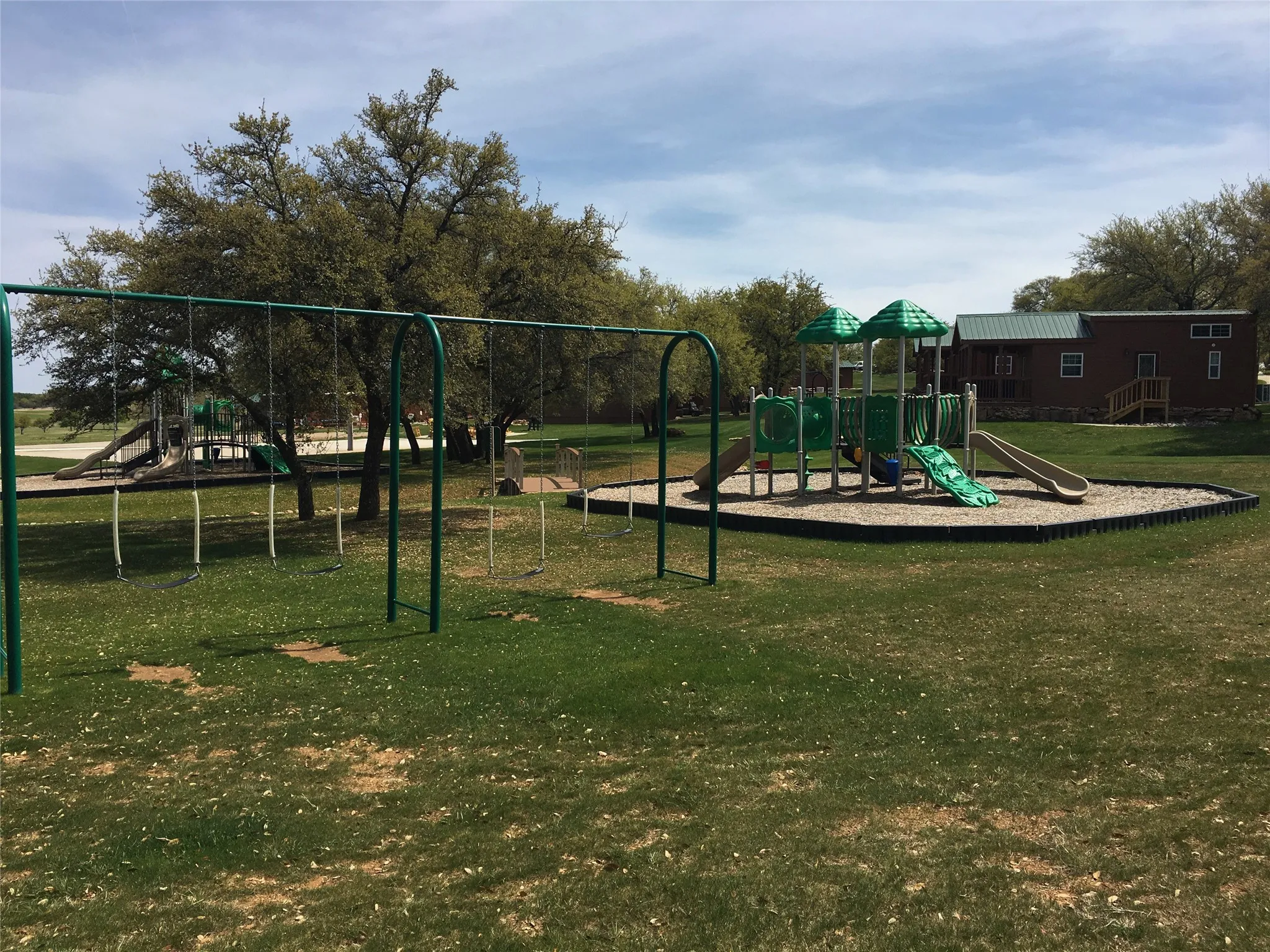 Expansive outdoor recreation area featuring a swing set, multi-level play structure with slides, and a tan bark play surface