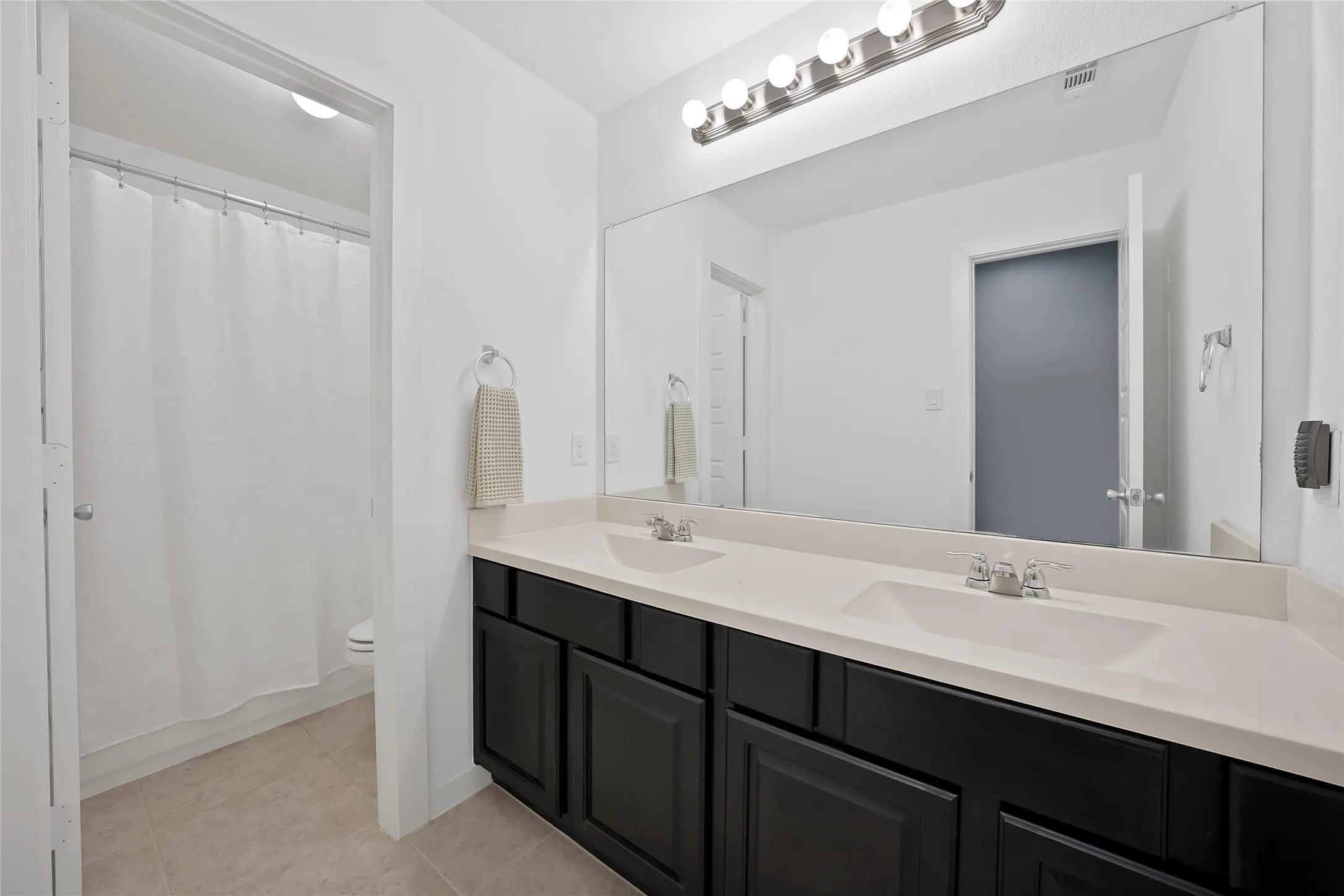 Bathroom featuring a dual vanity with dark cabinetry, light countertops, and chrome fixtures