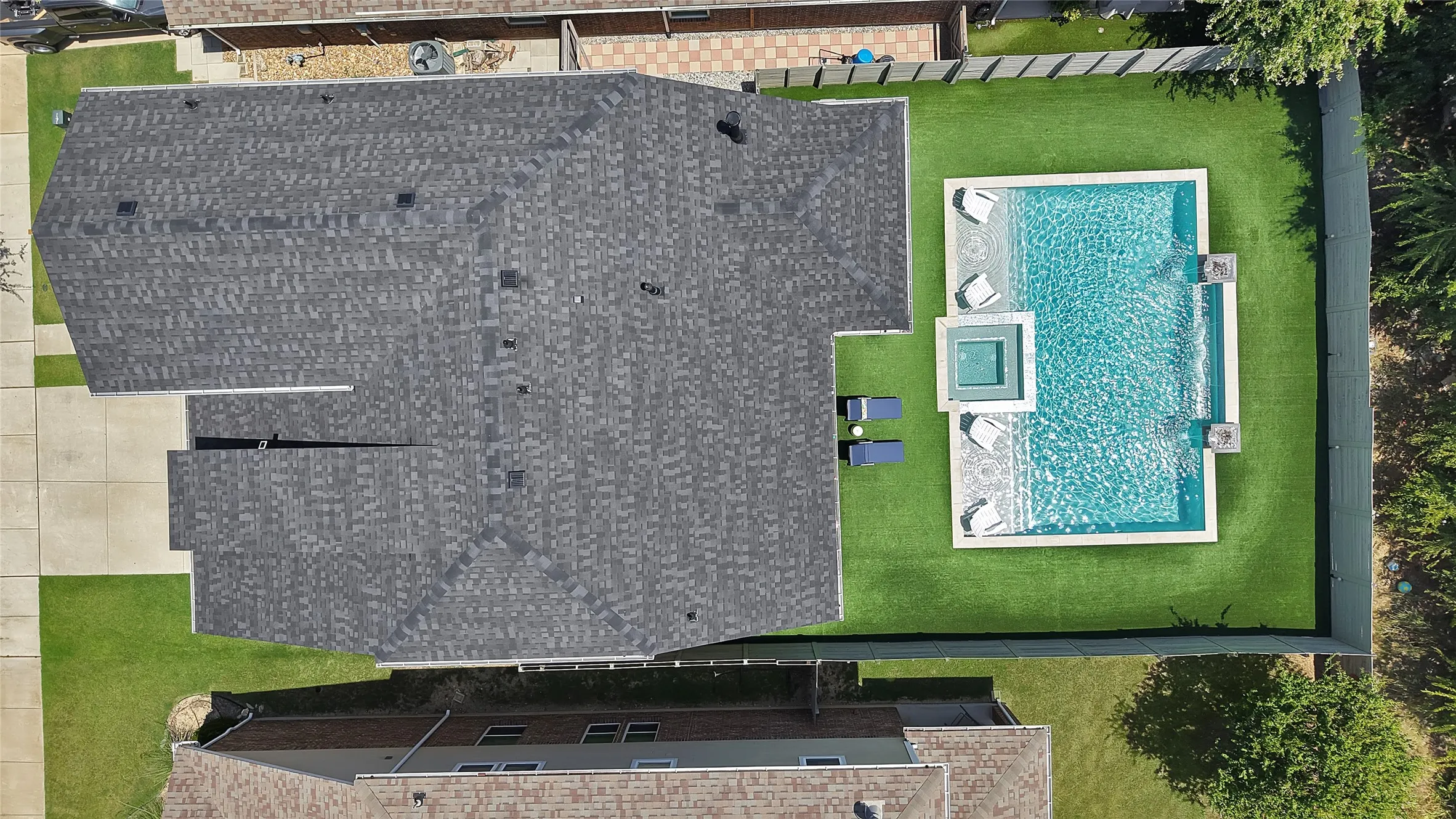 Backyard oasis featuring a rectangular swimming pool with integrated spa and water features, surrounded by artificial turf and a privacy fence