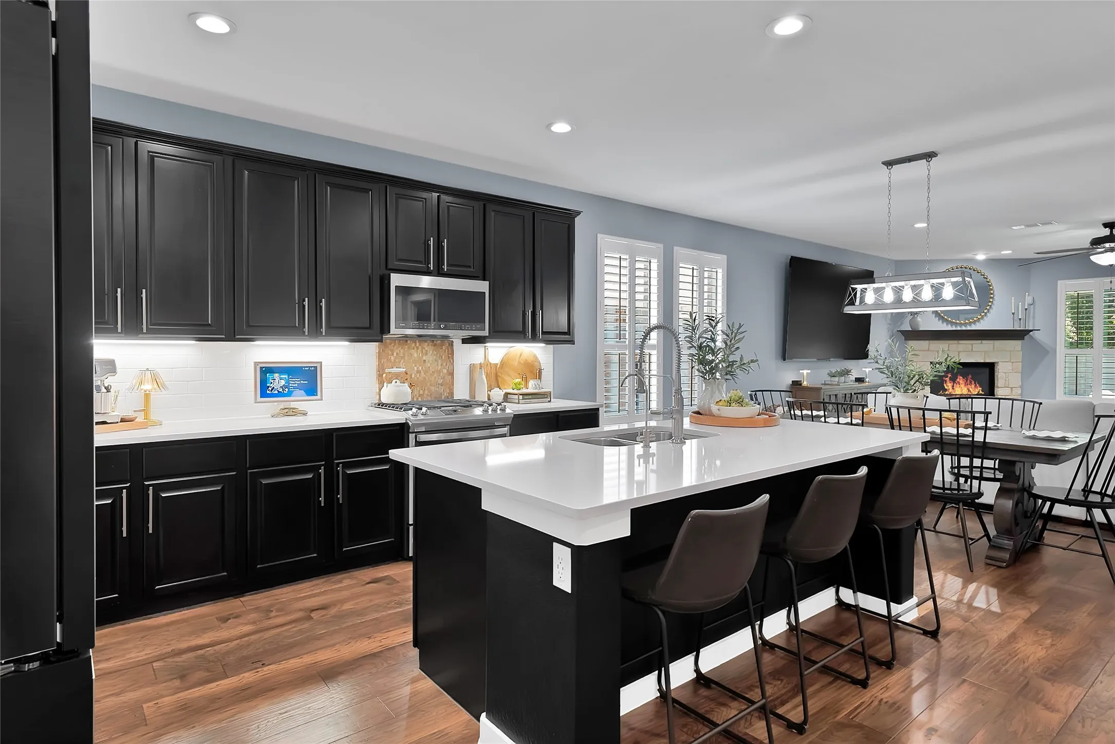Modern kitchen featuring an oversized island with seating, dark shaker cabinetry, stainless steel appliances, white subway tile backsplash, and wood-finish flooring