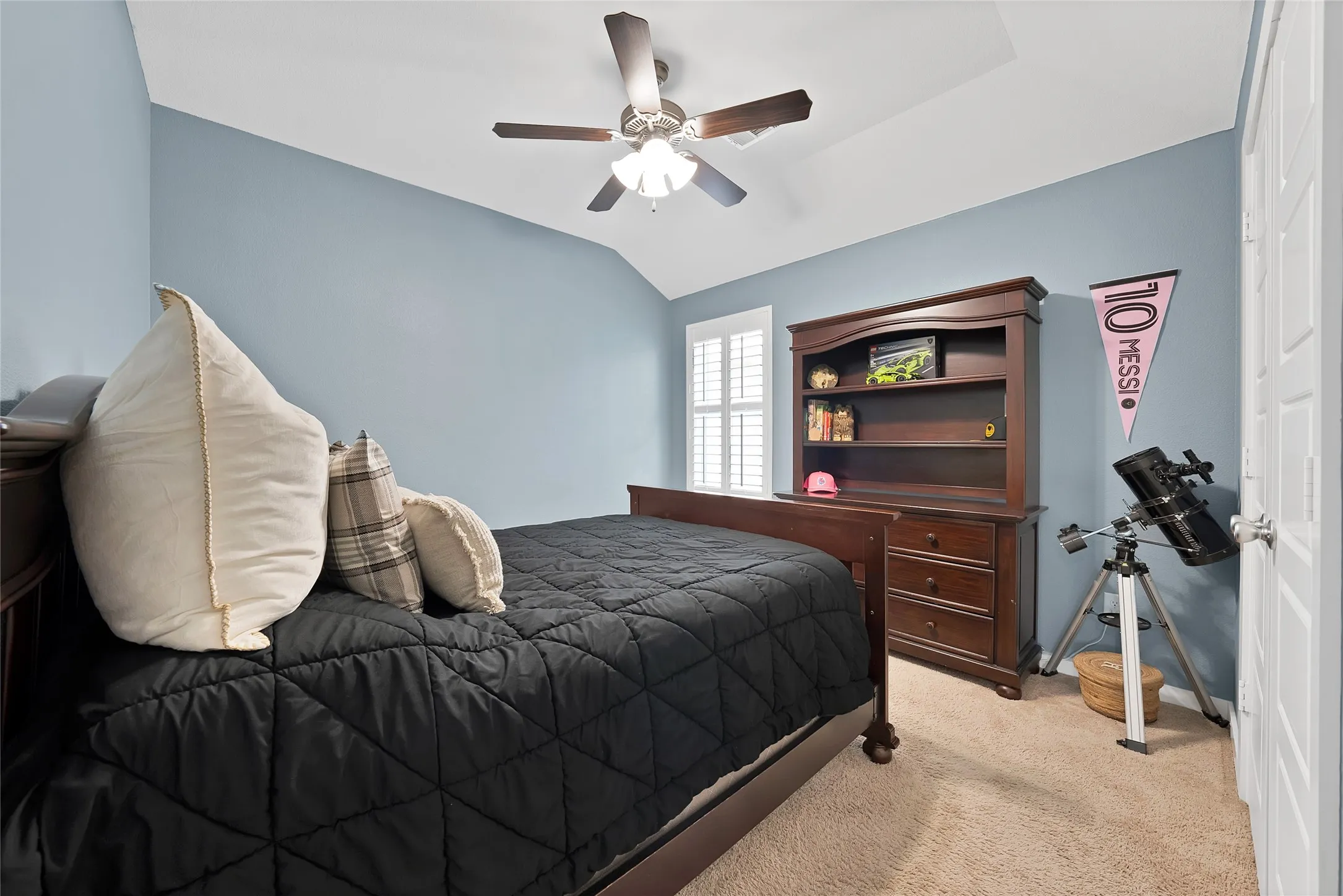 Vaulted ceiling room featuring a ceiling fan with light, plantation shutters, and light-toned carpet flooring