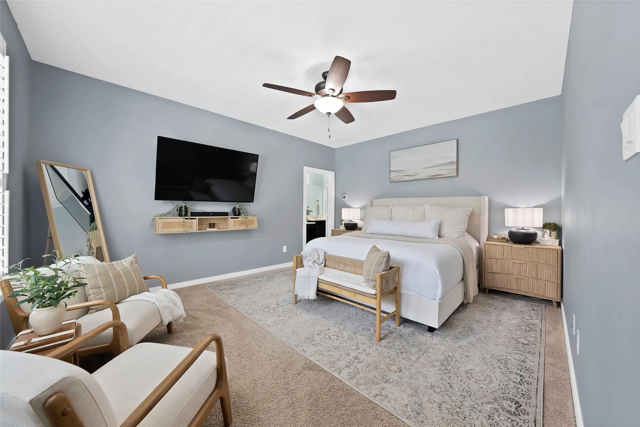 Spacious bedroom featuring light blue walls, wood-finish ceiling fan, and carpet flooring