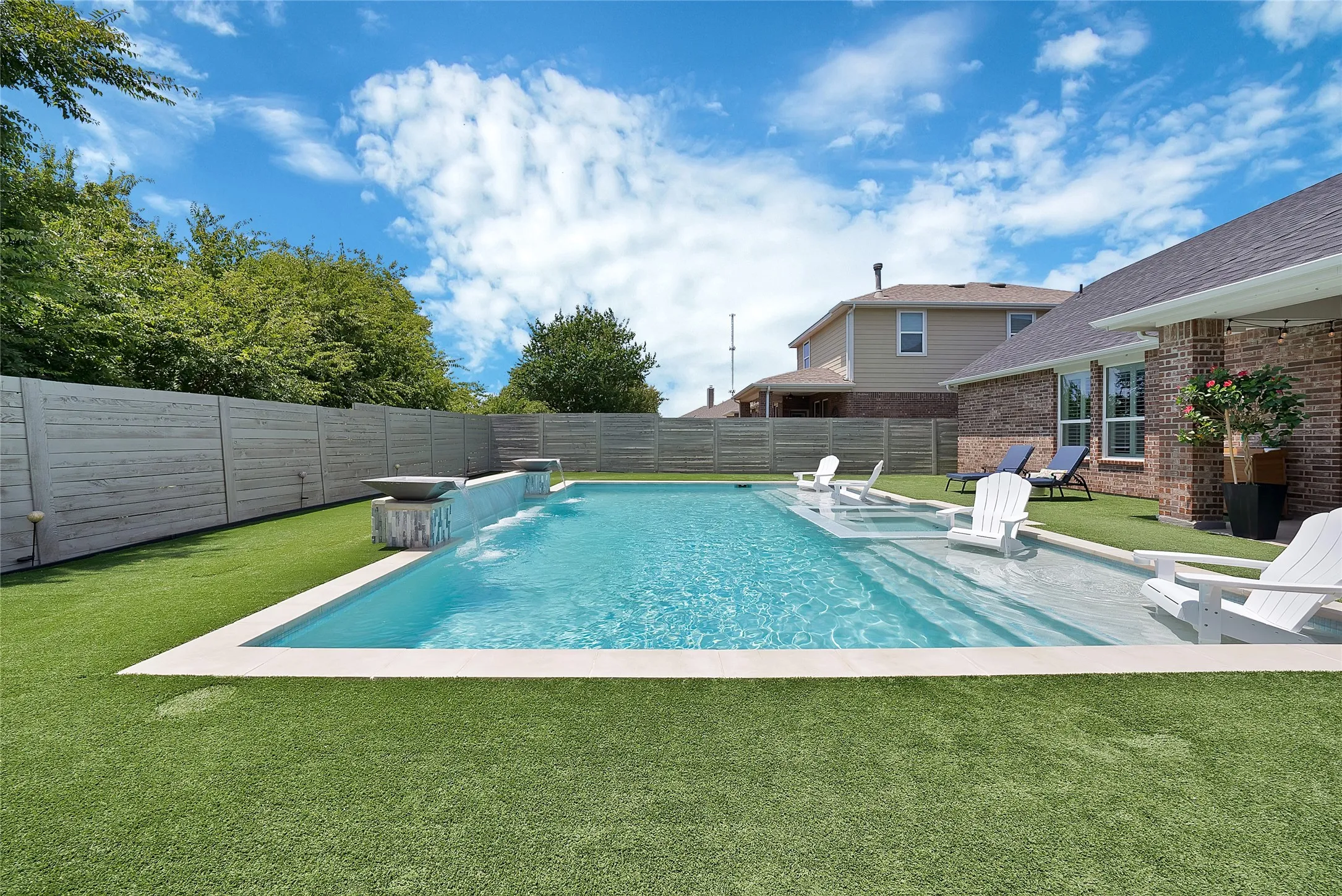 Backyard oasis featuring a rectangular swimming pool with integrated tanning ledge and water features