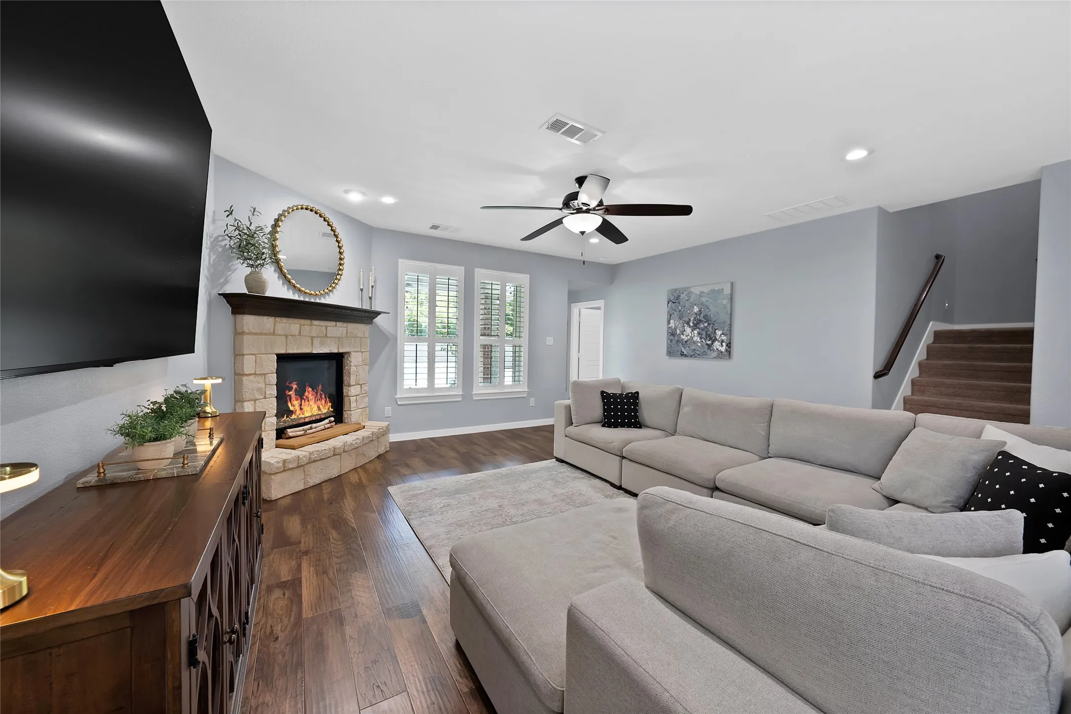 Living area featuring wood-finish flooring, a stone-faced corner fireplace with a dark mantel, and plantation shutters on the windows
