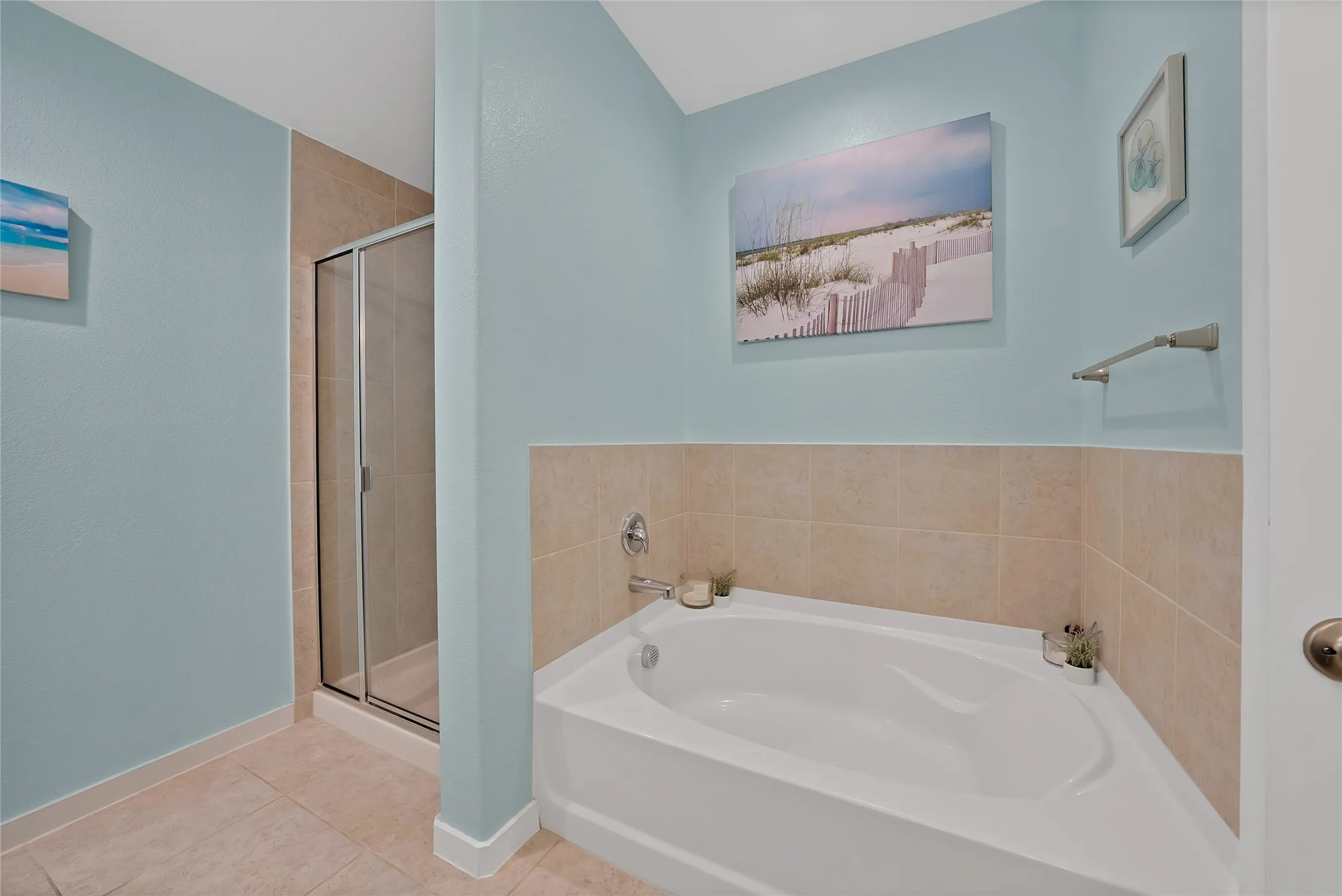 Corner garden tub with tile surround, glass-enclosed shower, light blue painted walls, and tile flooring