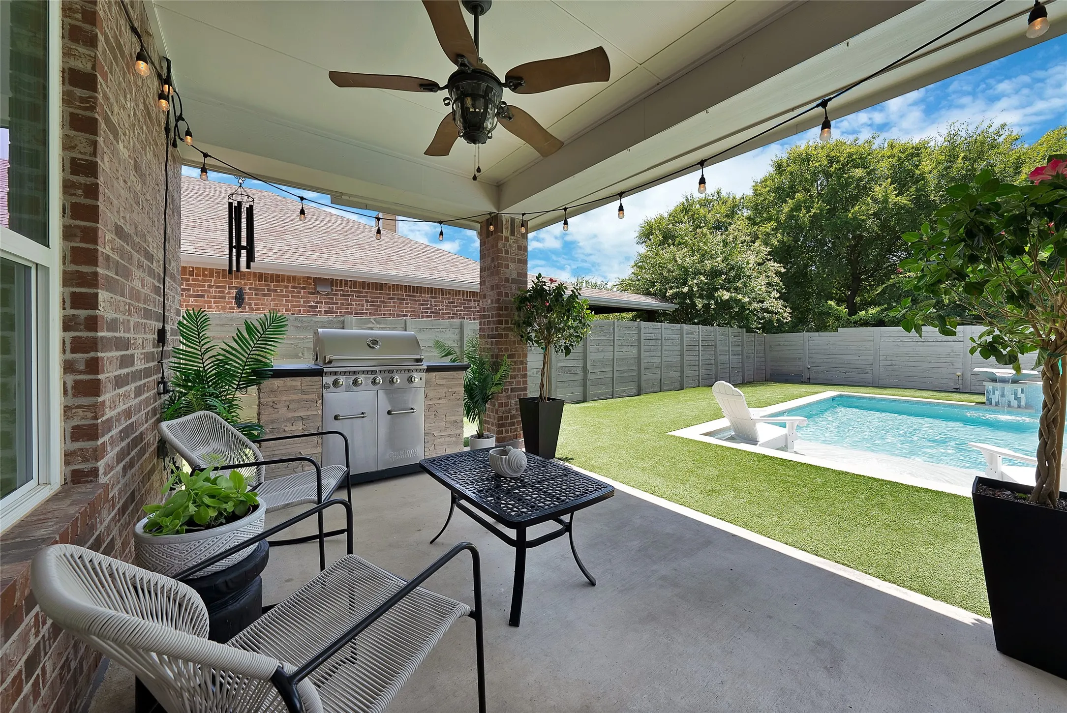 Covered patio featuring a ceiling fan, string lighting, and an outdoor kitchen with a built-in grill and stone base
